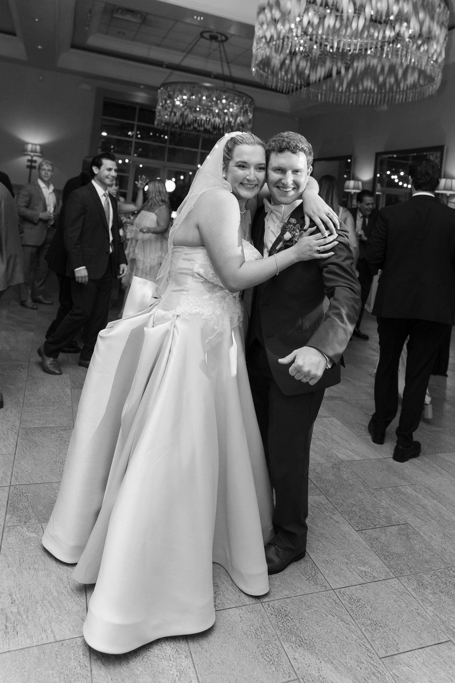 Black and white photo of smiling bride and groom embracing on the wedding reception dance floor.
