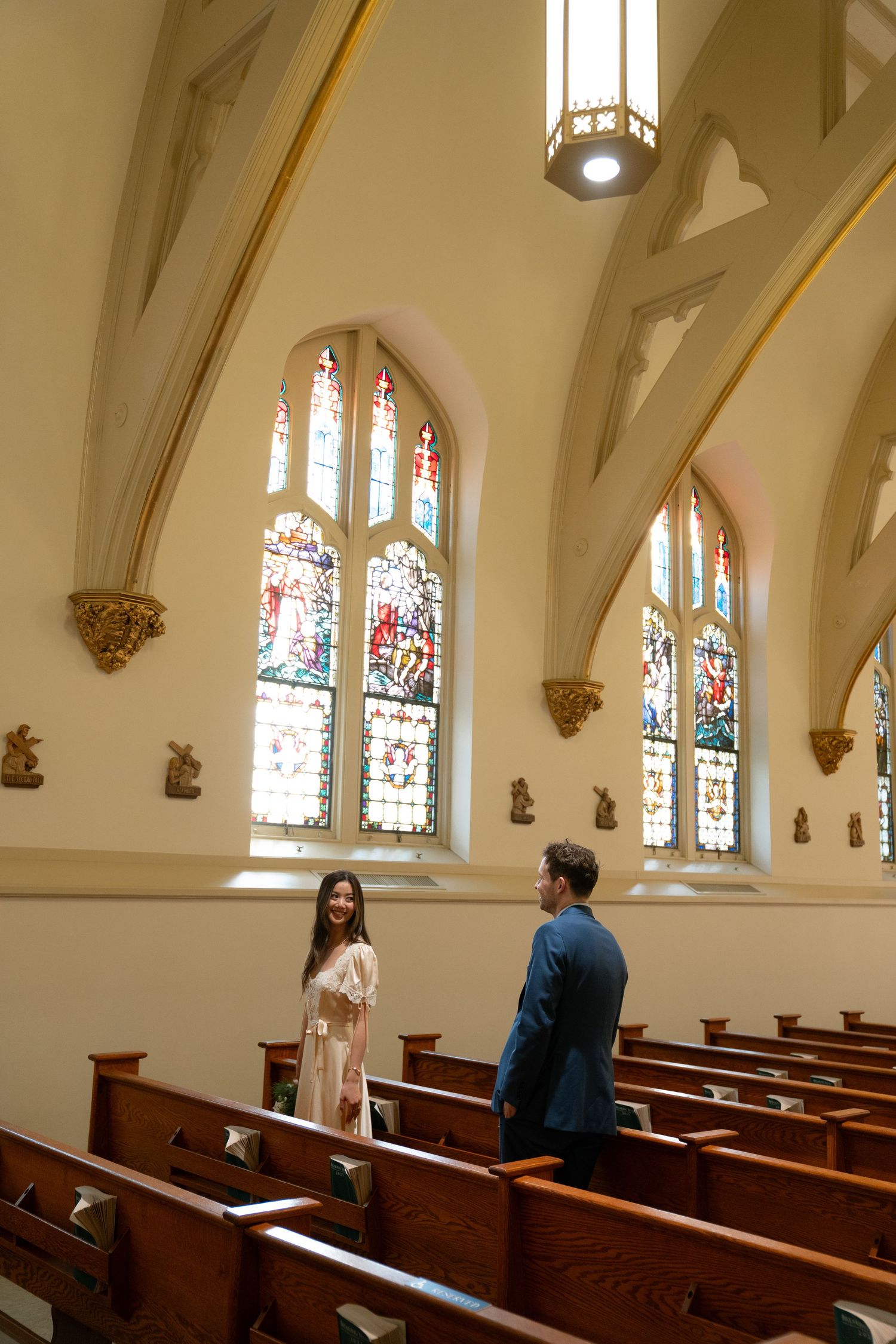 Two people stand in conversation inside a church sanctuary with stained glass windows and wooden pews.