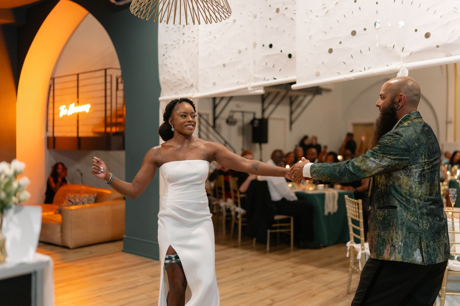 A couple shares an intimate dance at an indoor wedding reception venue with warm lighting and hardwood floors.