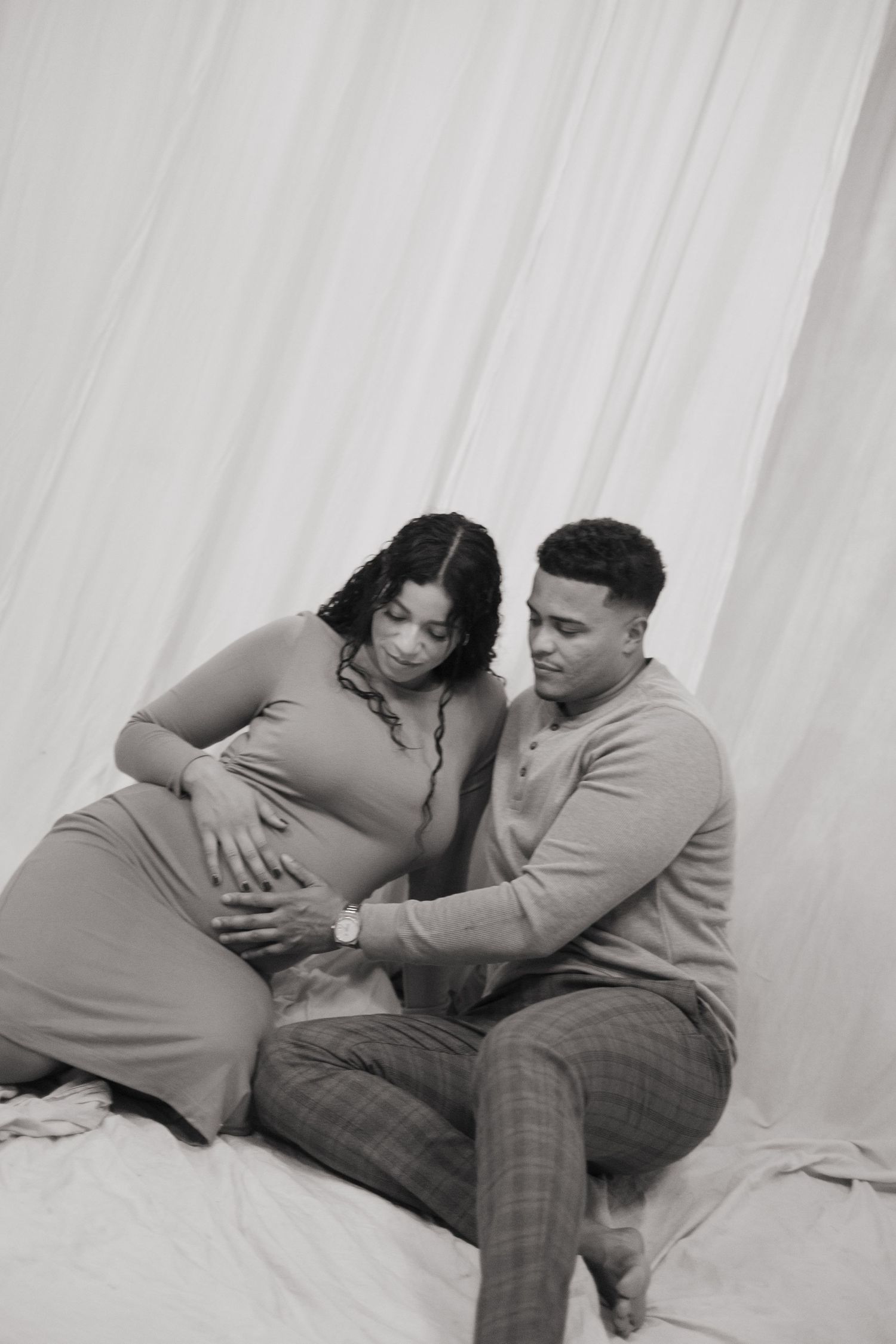 Black and white maternity photo of a couple sitting together, man tenderly touching pregnant woman's belly.