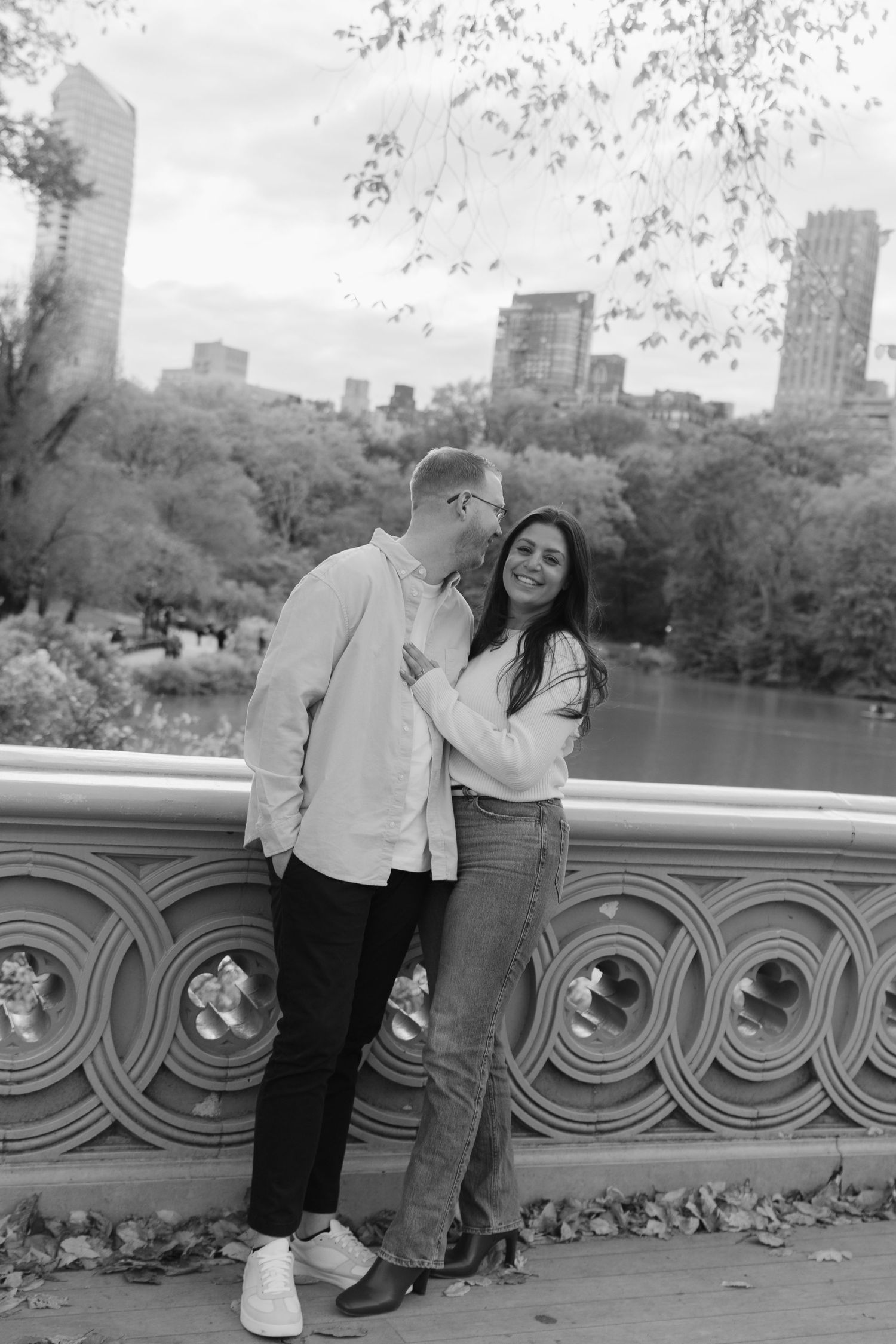A couple shares a joyful moment on a bridge overlooking Central Park with the NYC skyline in the background.