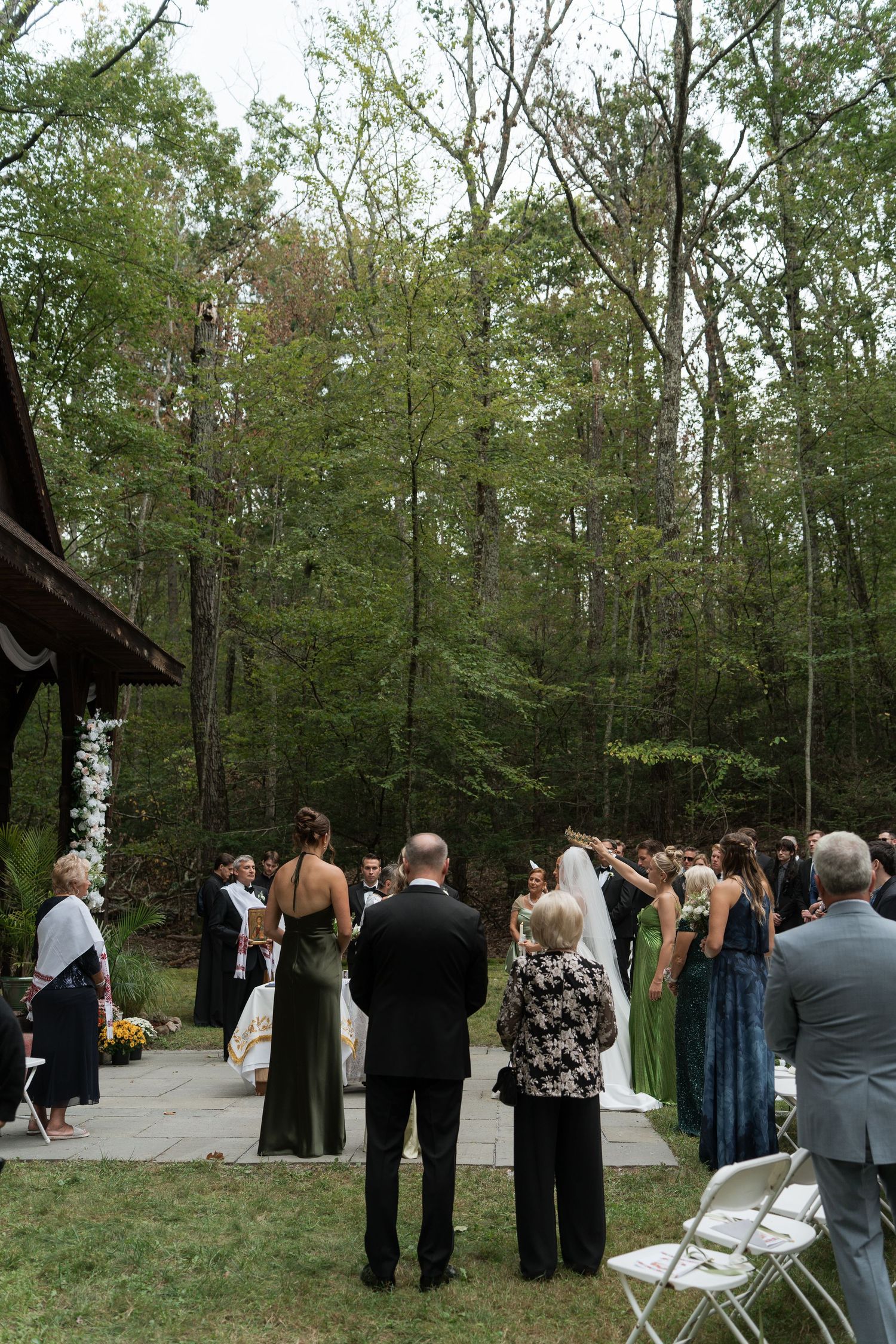 Outdoor woodland wedding ceremony with guests standing as bride walks down the aisle toward the altar.