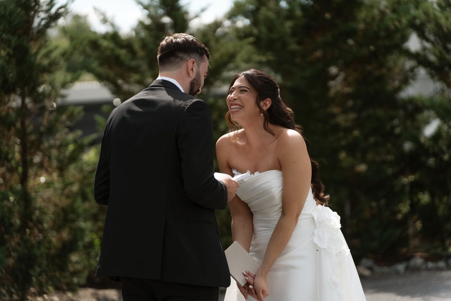 Bride in strapless white gown laughing joyfully with groom during outdoor wedding first look.