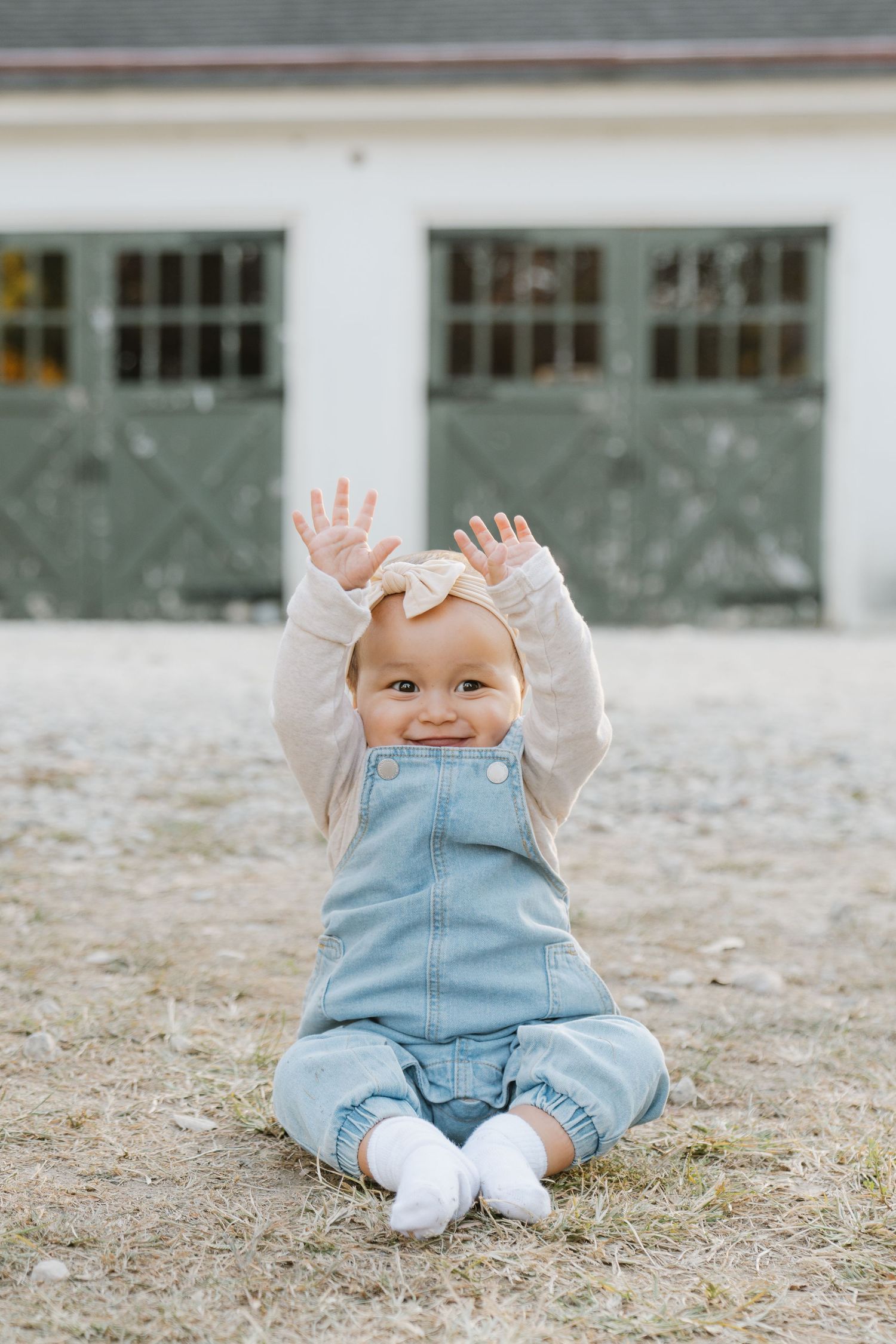A small child in denim overalls and beige sweater sits on the ground in a sequence of playful poses.