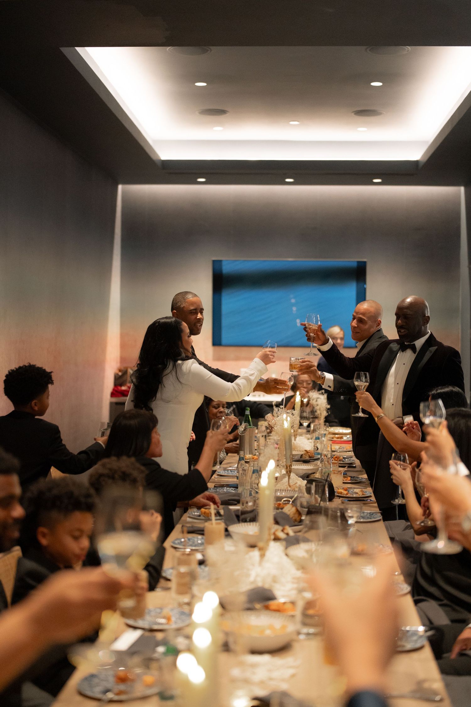 Guests raise glasses in a toast during an intimate dinner celebration in a modern venue.