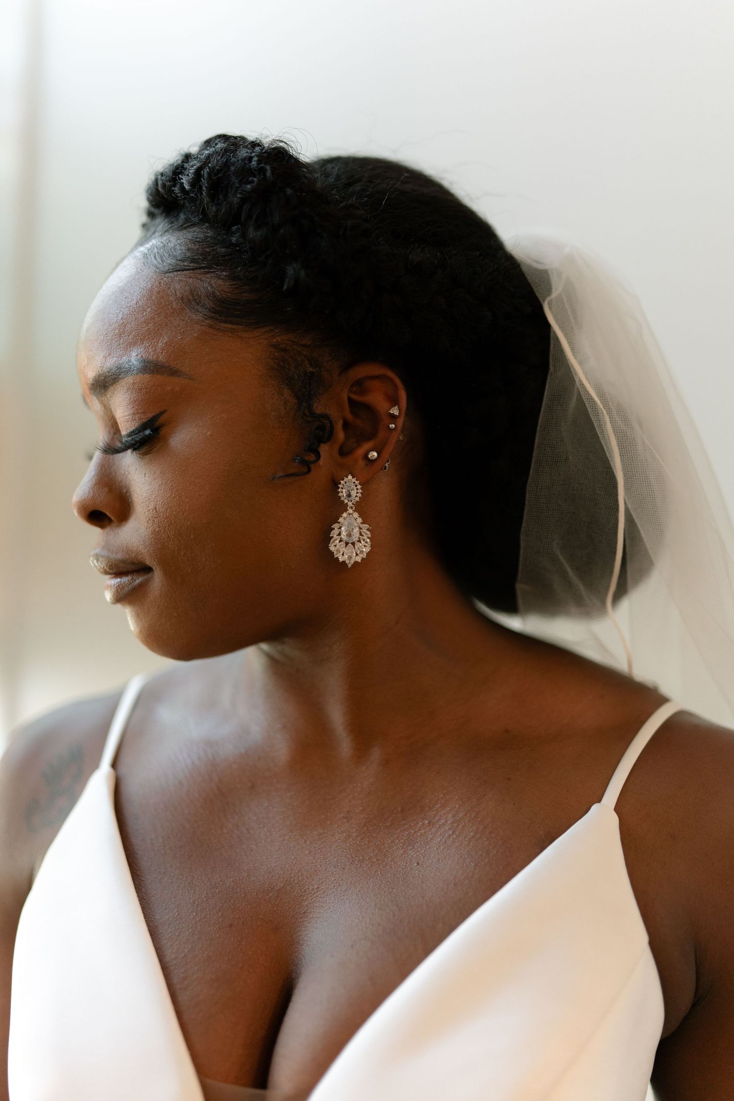 Close-up profile view of bride wearing crystal drop earrings and white wedding dress with veil.