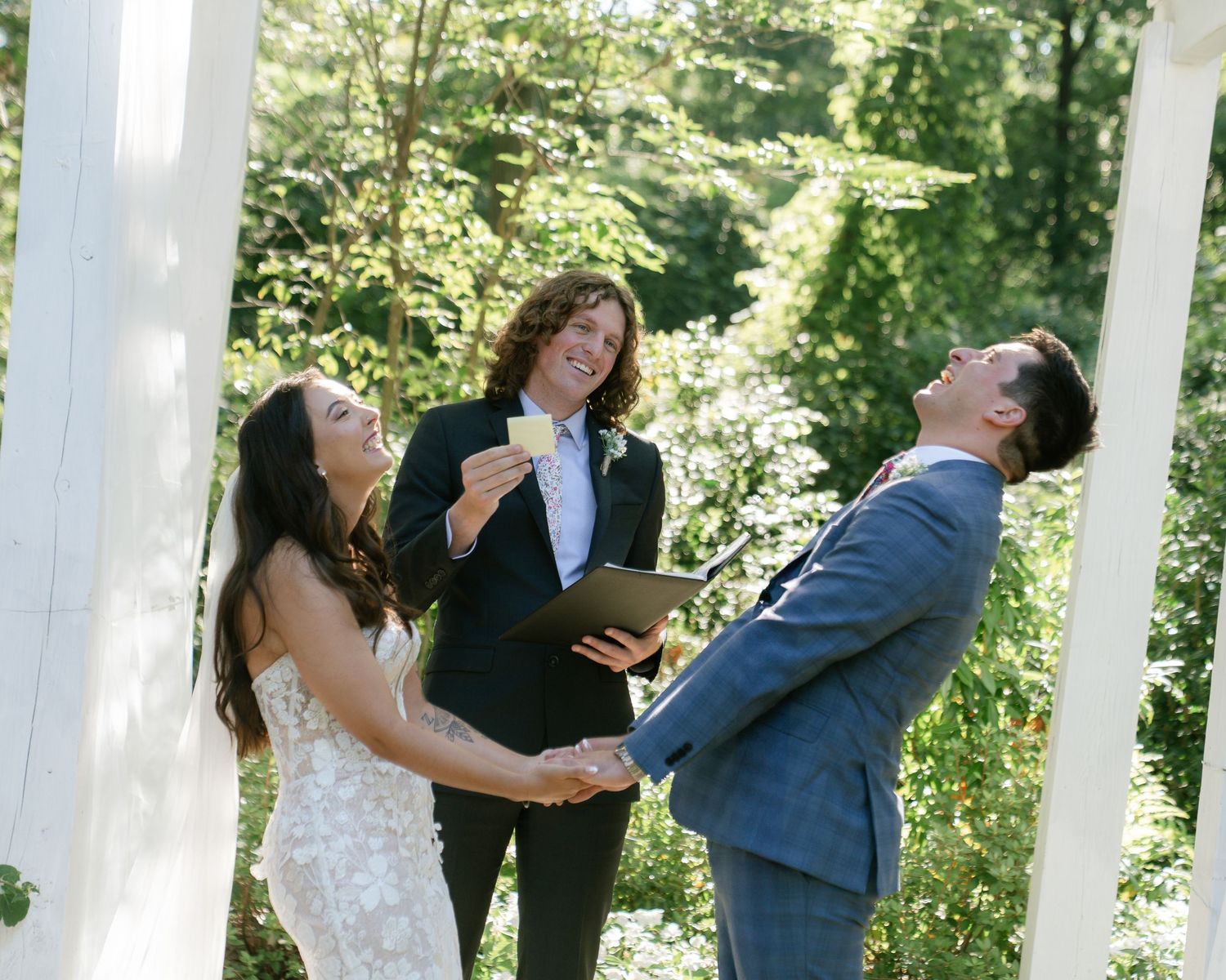 A couple sharing a romantic moment under a white outdoor pergola surrounded by lush greenery.