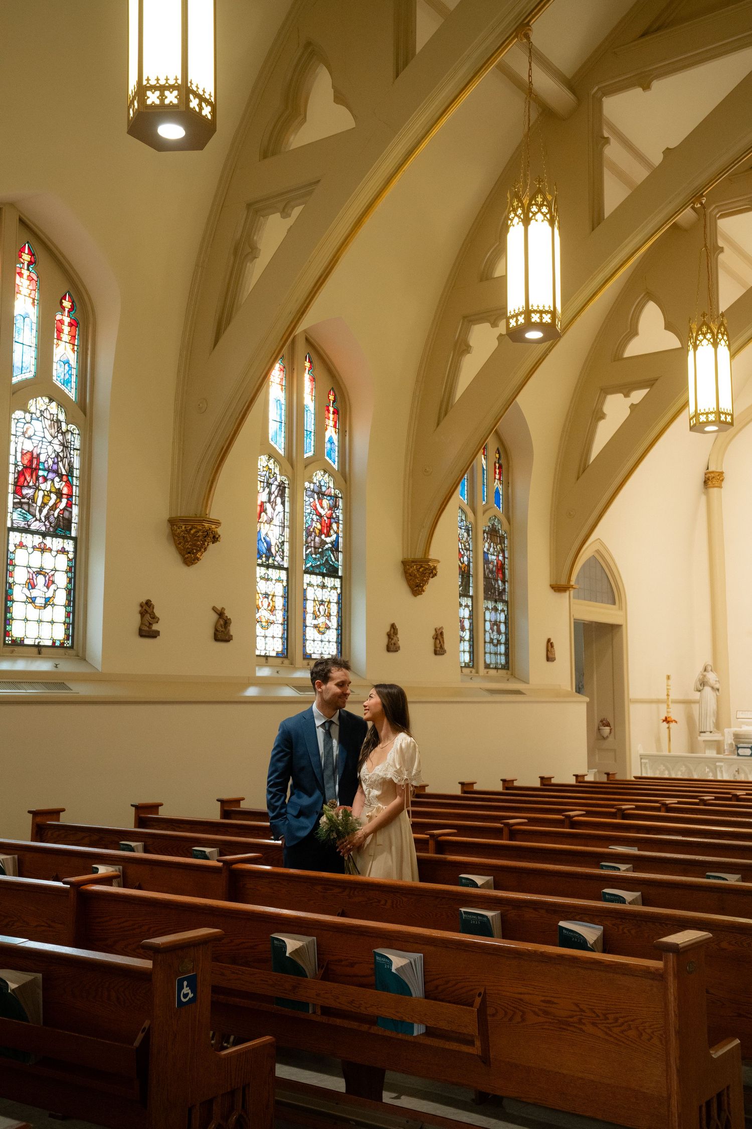 A couple stands together in a church aisle with Gothic architecture and warm lighting.