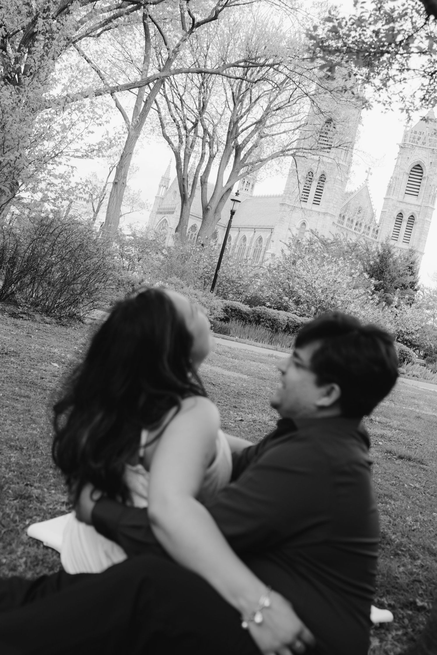 A couple shares an intimate black and white moment in a park setting.