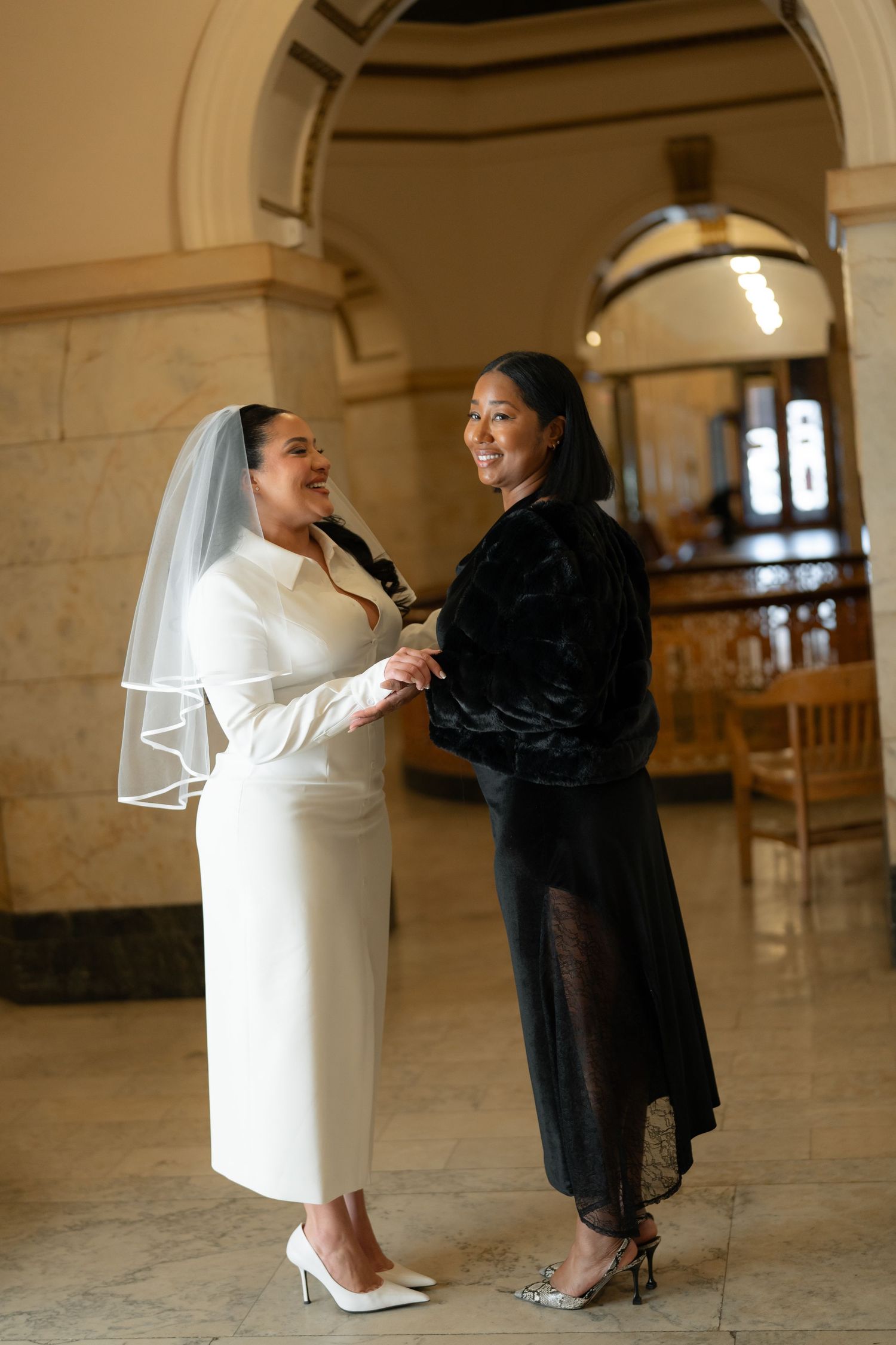 Two people in contrasting white and black outfits share an intimate moment in an ornate hallway.