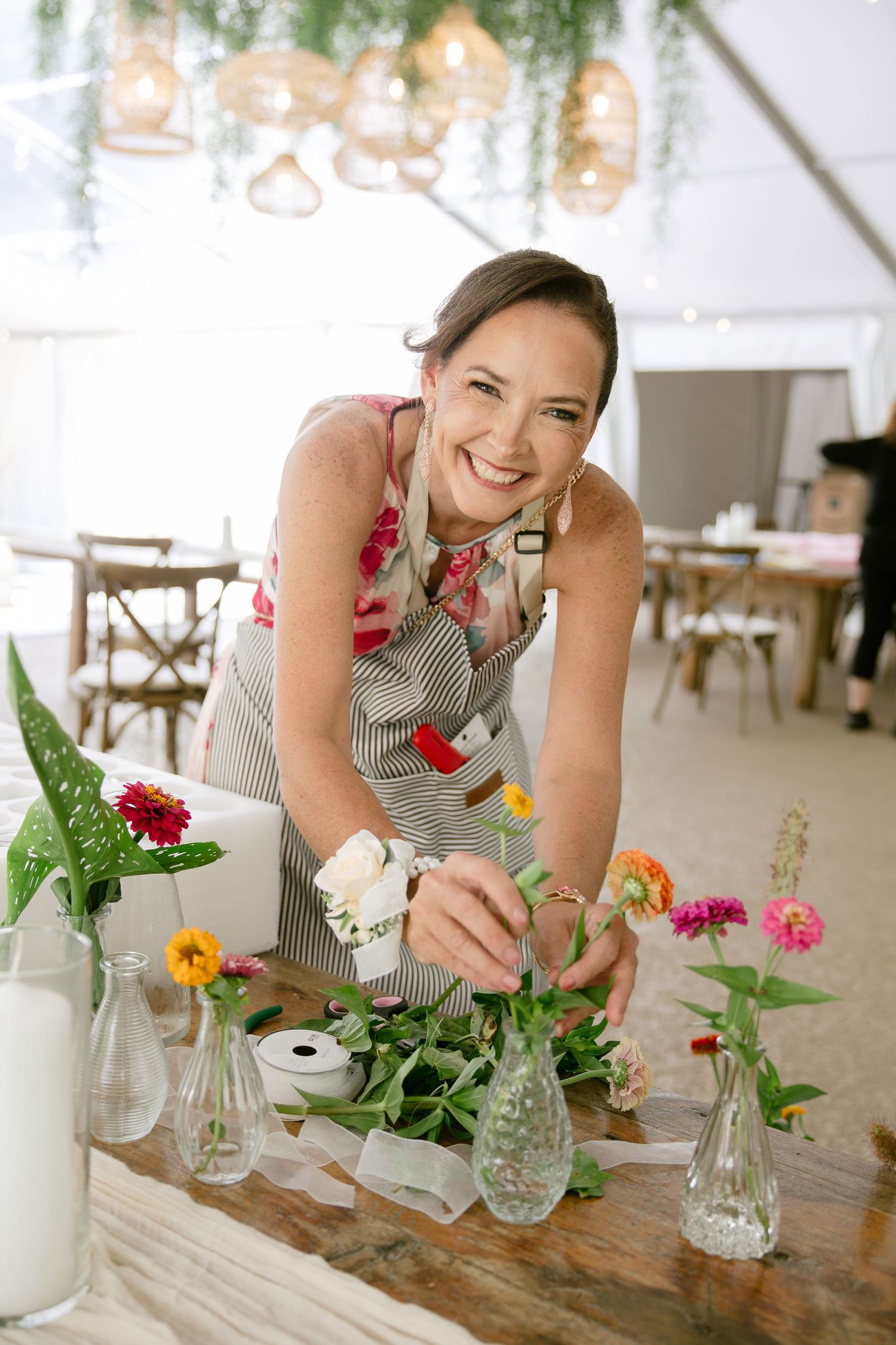 Person arranging colorful flowers in glass vases on a rustic wooden table.