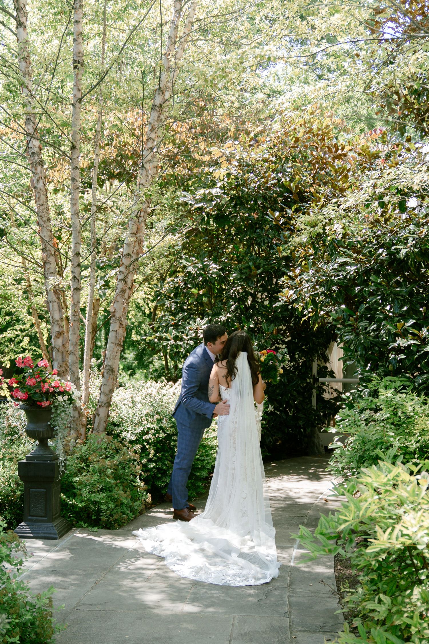 Couple embraces during first look moment in garden surrounded by birch trees and greenery.