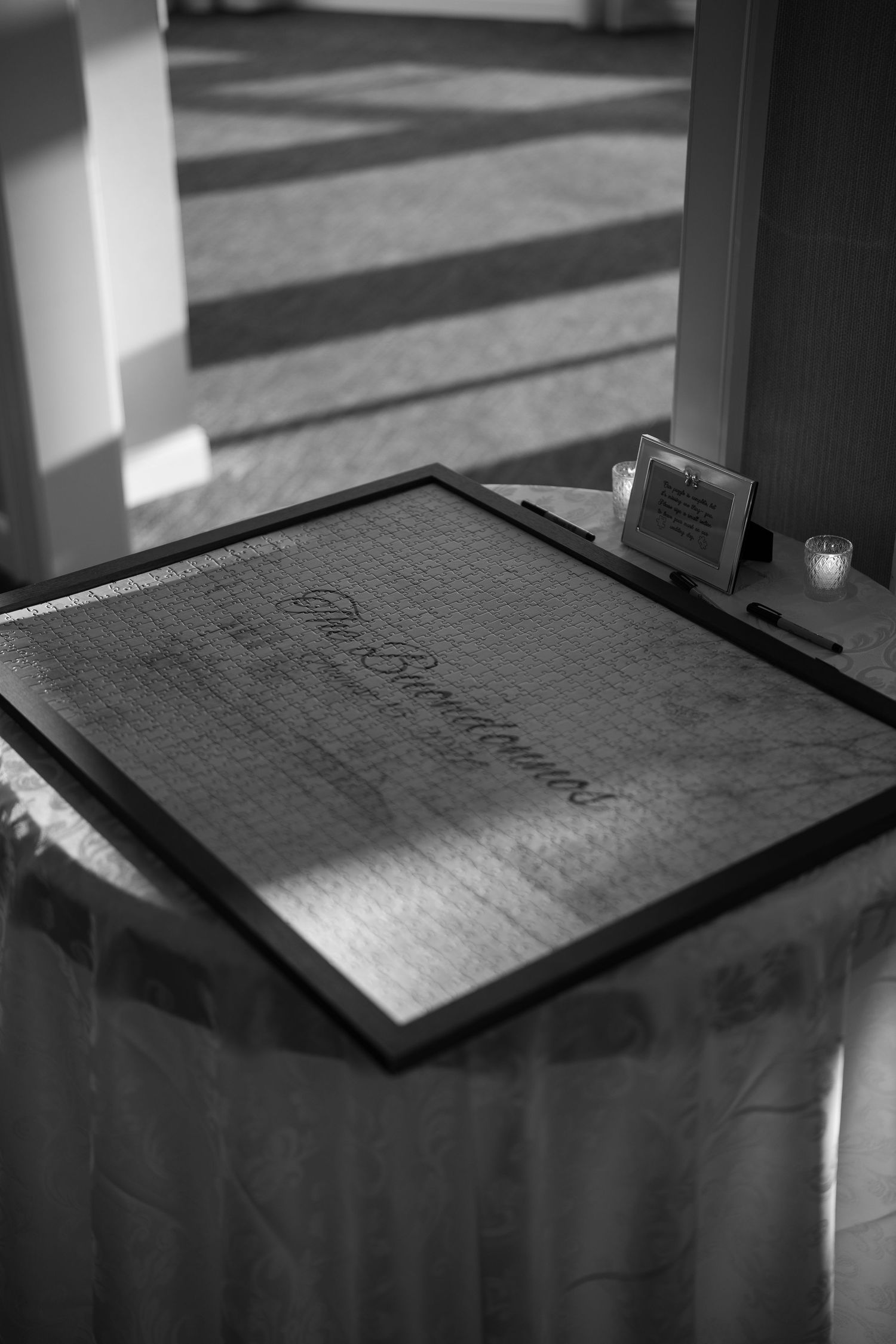 Elegant black and white photo of a framed wedding guest signature board on a draped table.