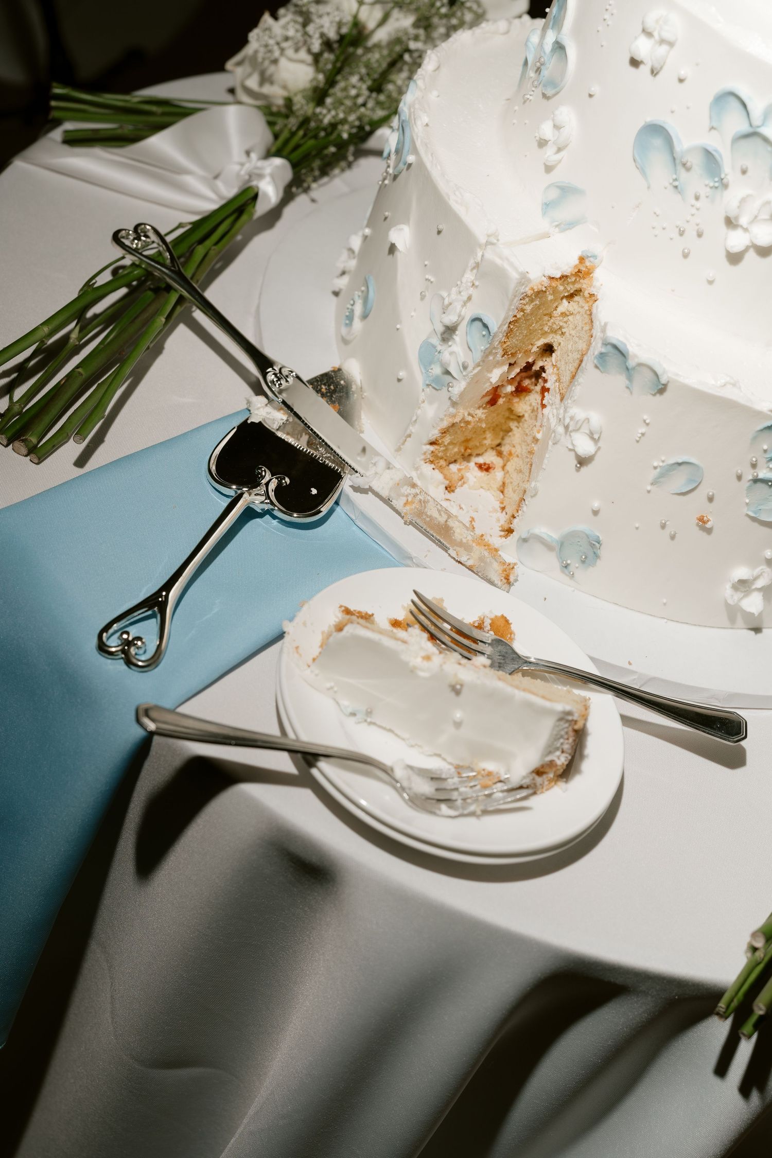 Sliced white wedding cake with blue watercolor details on a table with silver cake server.