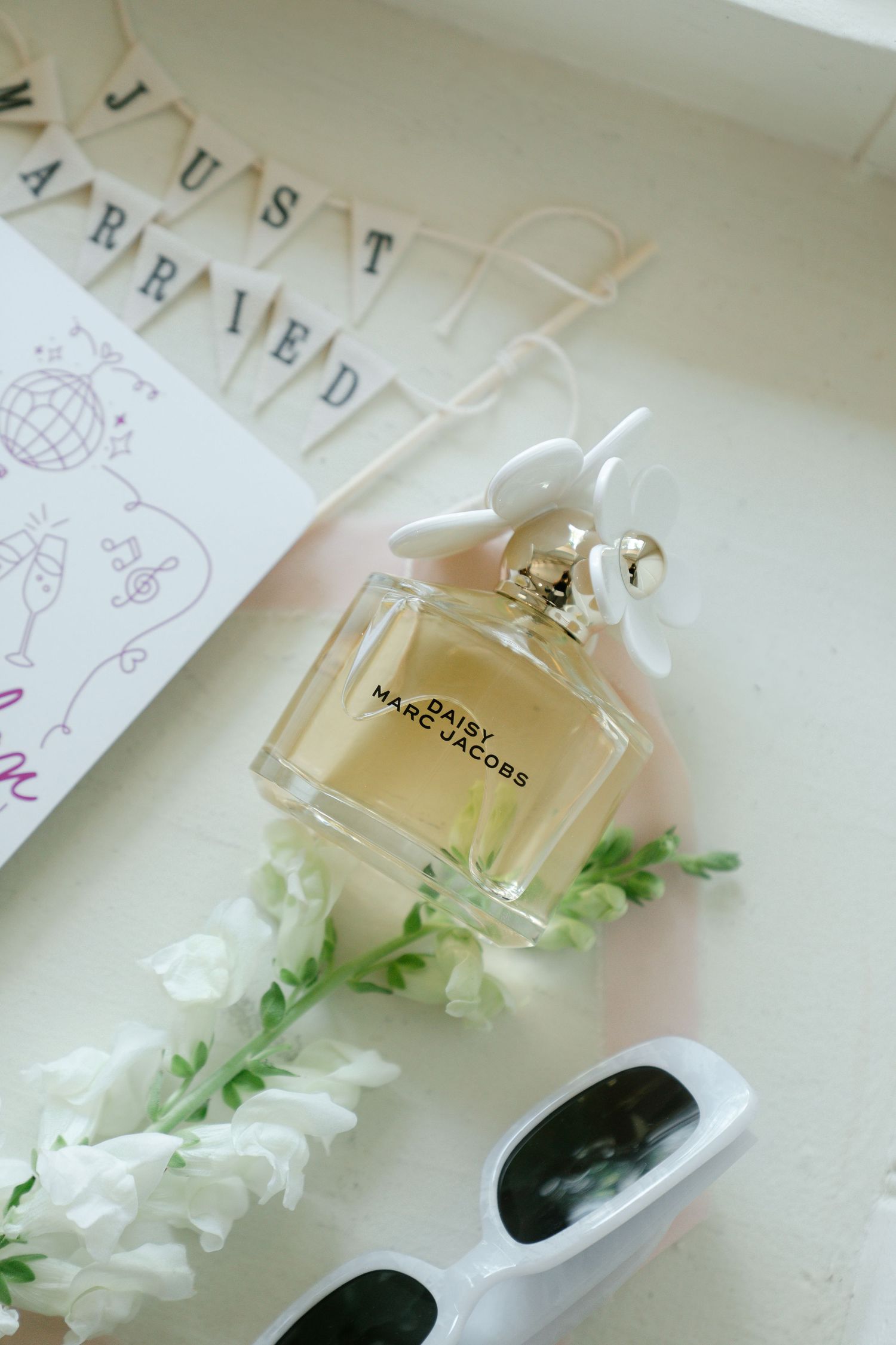 Perfume bottles and white flowers arranged elegantly on a light surface with sketched artwork in the background.