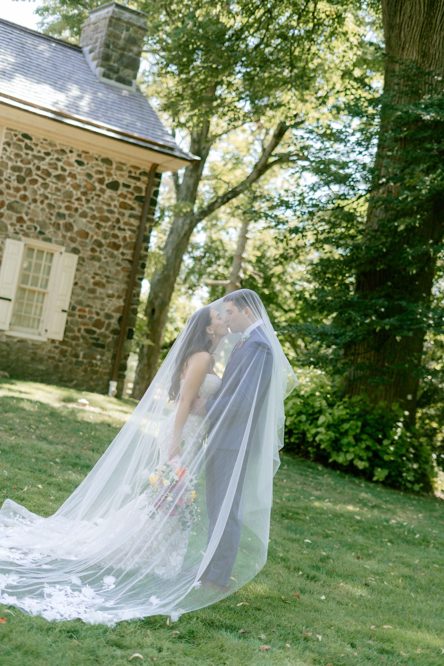 A flowing white wedding veil catches the breeze against a stone building backdrop.