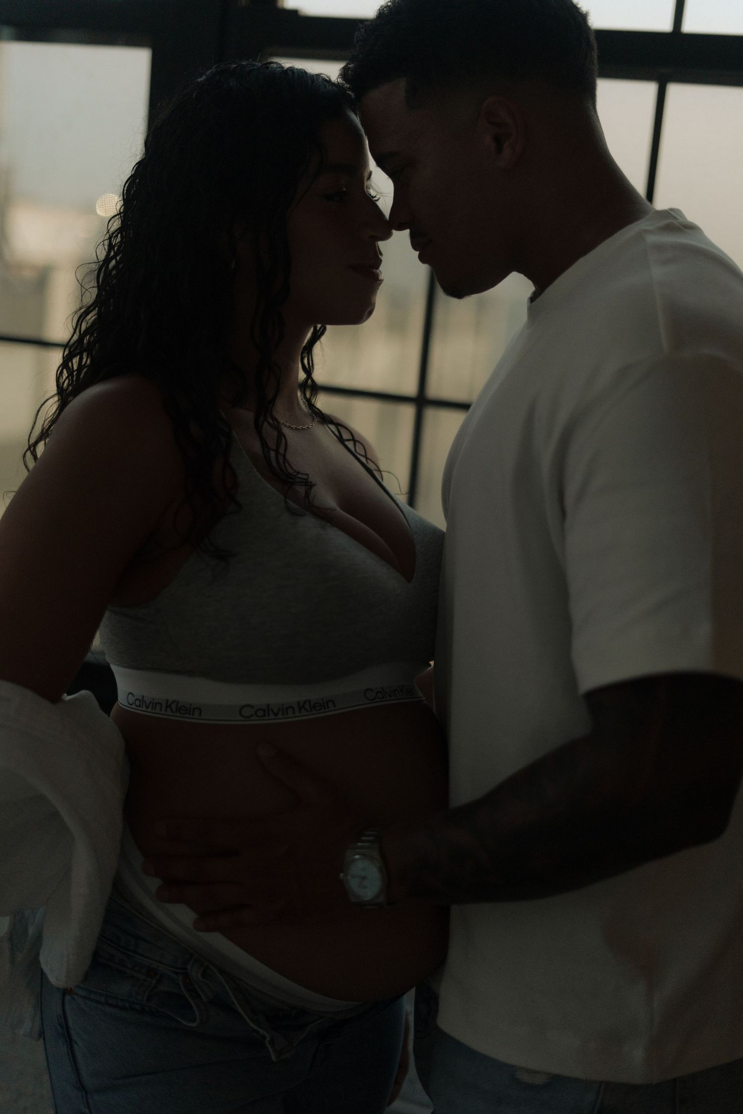 Silhouetted couple in intimate pose against window light.