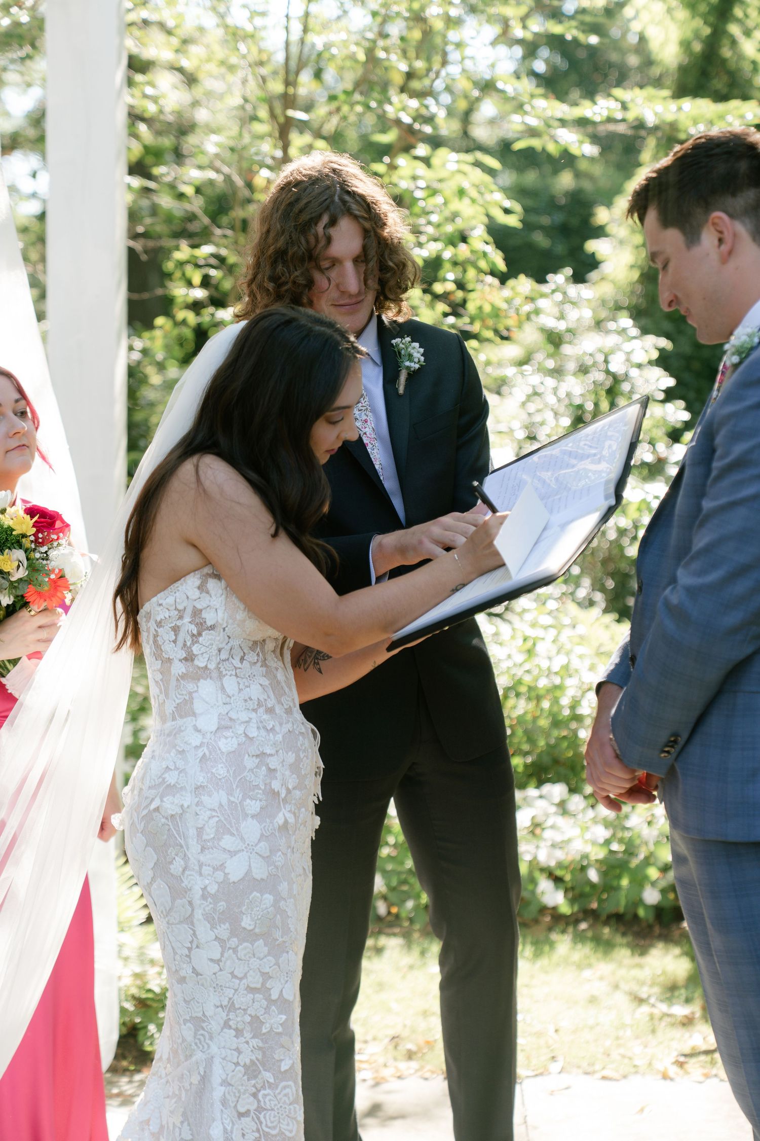 Outdoor wedding ceremony under white gazebo with pink floral arrangements.