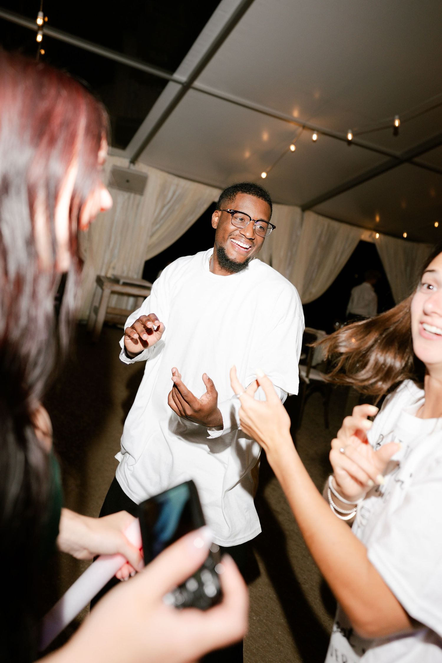 People dancing and celebrating at nighttime party under tent lighting.