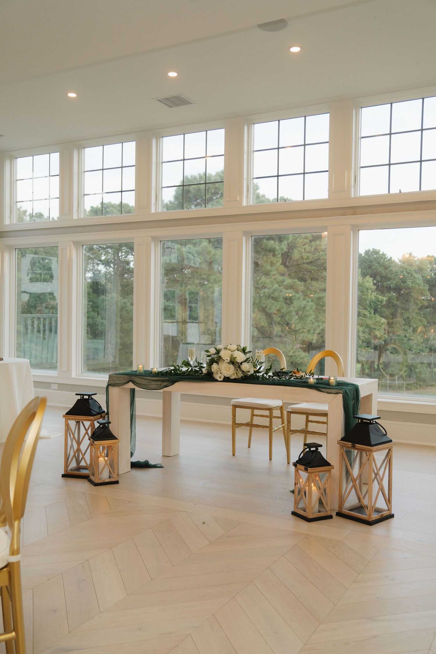Elegant event space with white walls, large windows, hardwood floors and decorative lanterns arranged throughout the room.