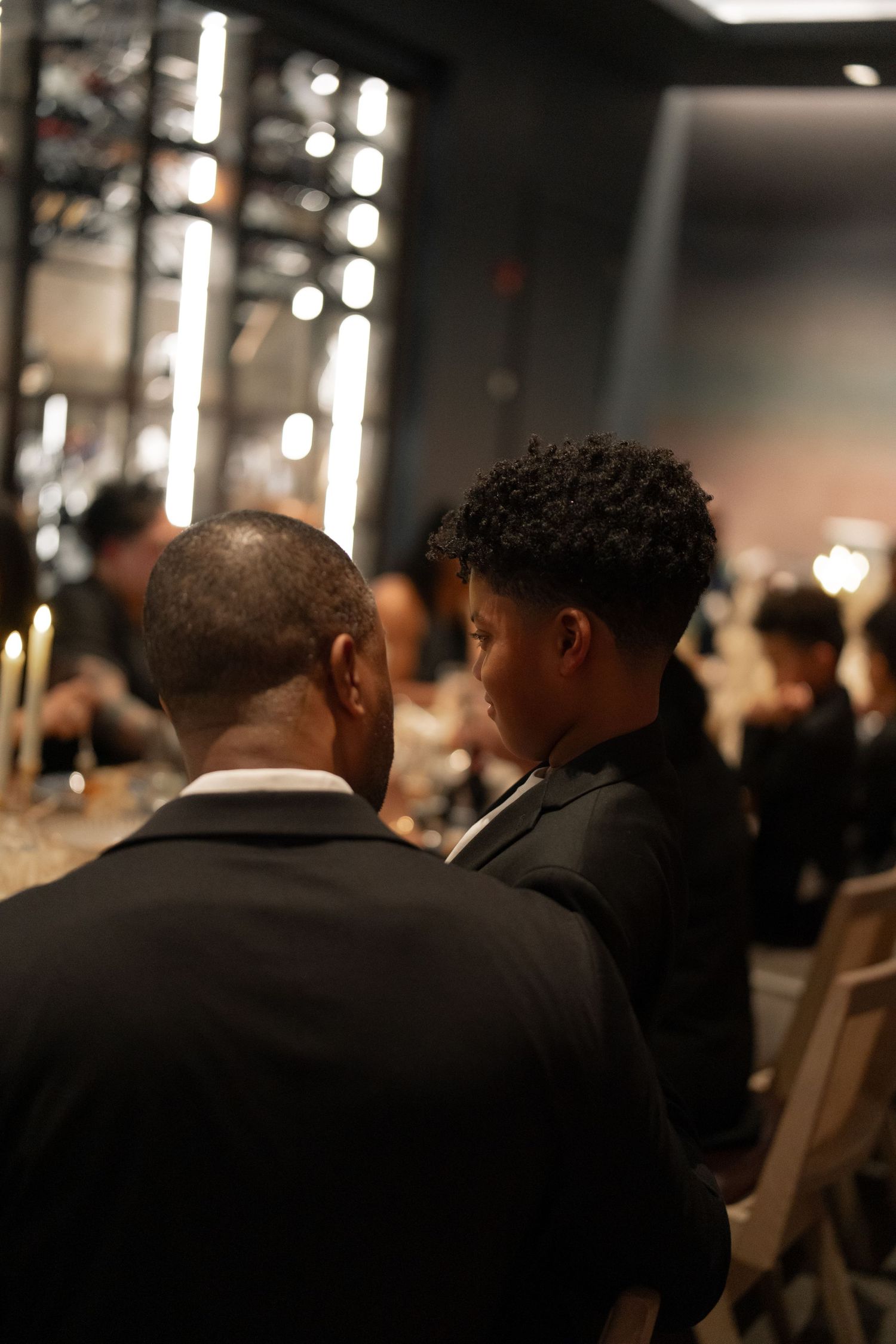 Silhouettes of people seated at formal dinner event with ambient lighting in background.