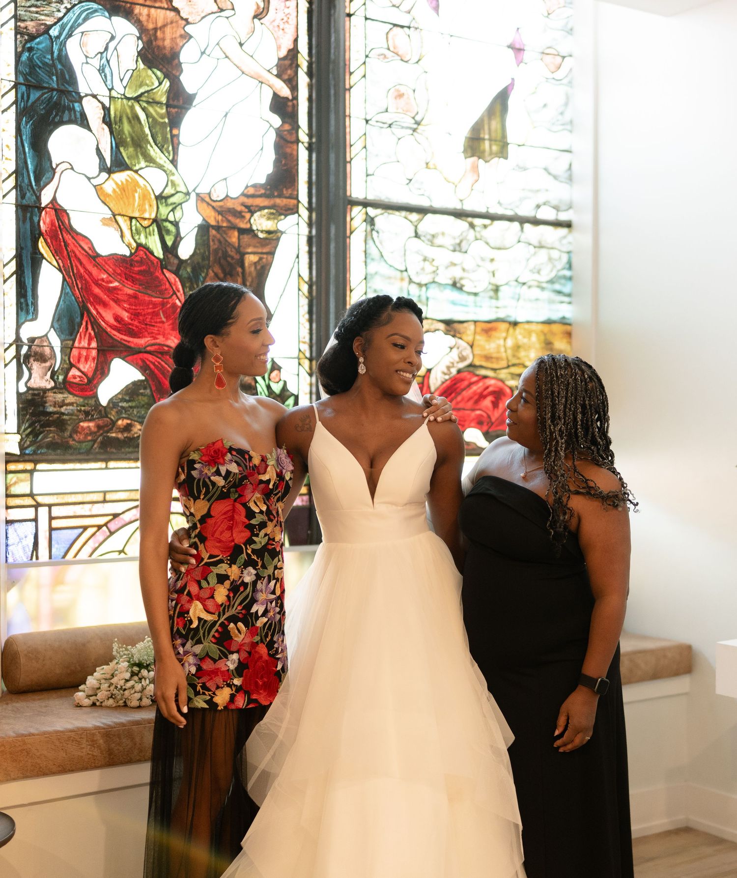 Wedding party poses together in front of colorful stained glass window during celebration.