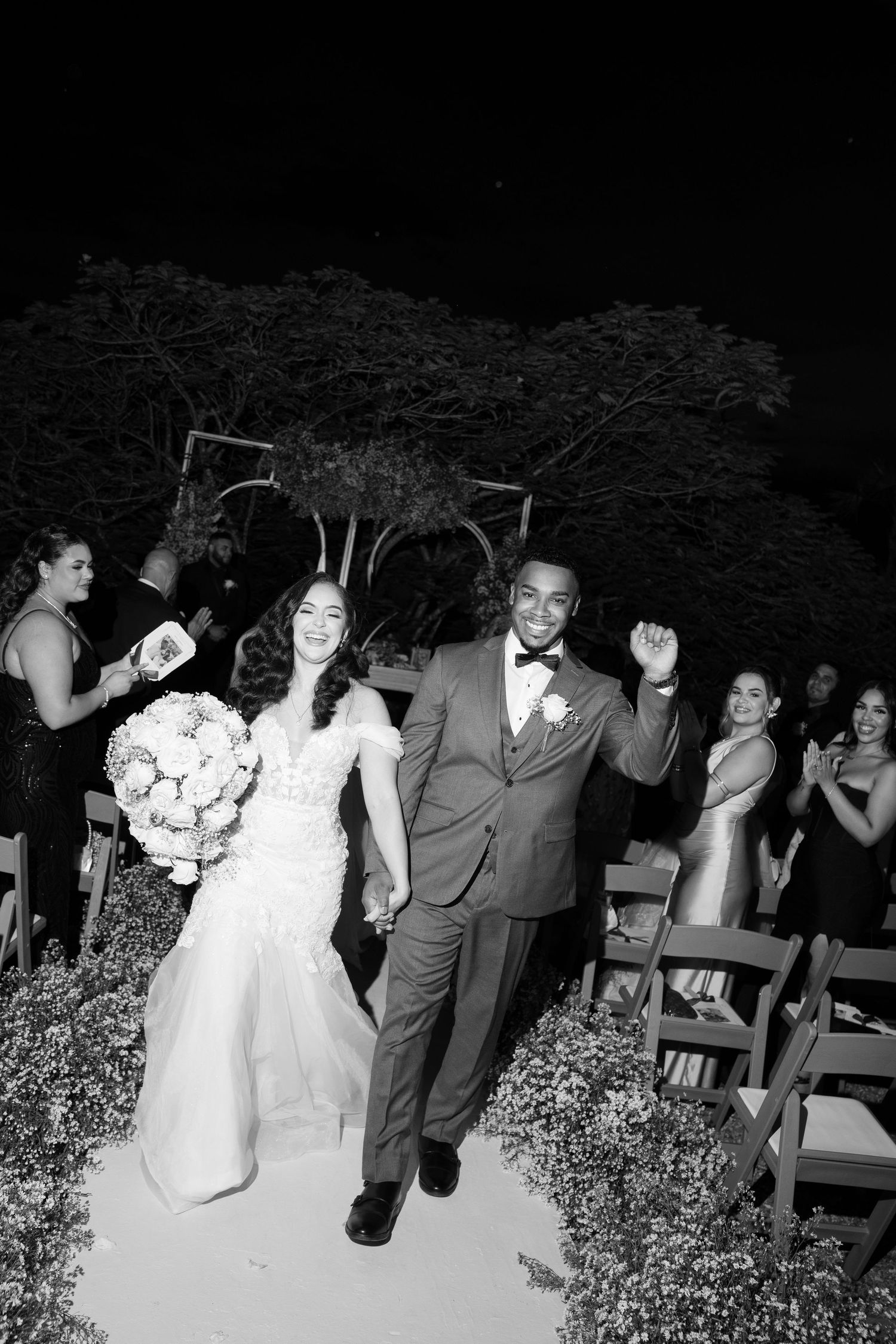 A joyful wedding couple walks down the aisle together after their ceremony as guests celebrate in the background.