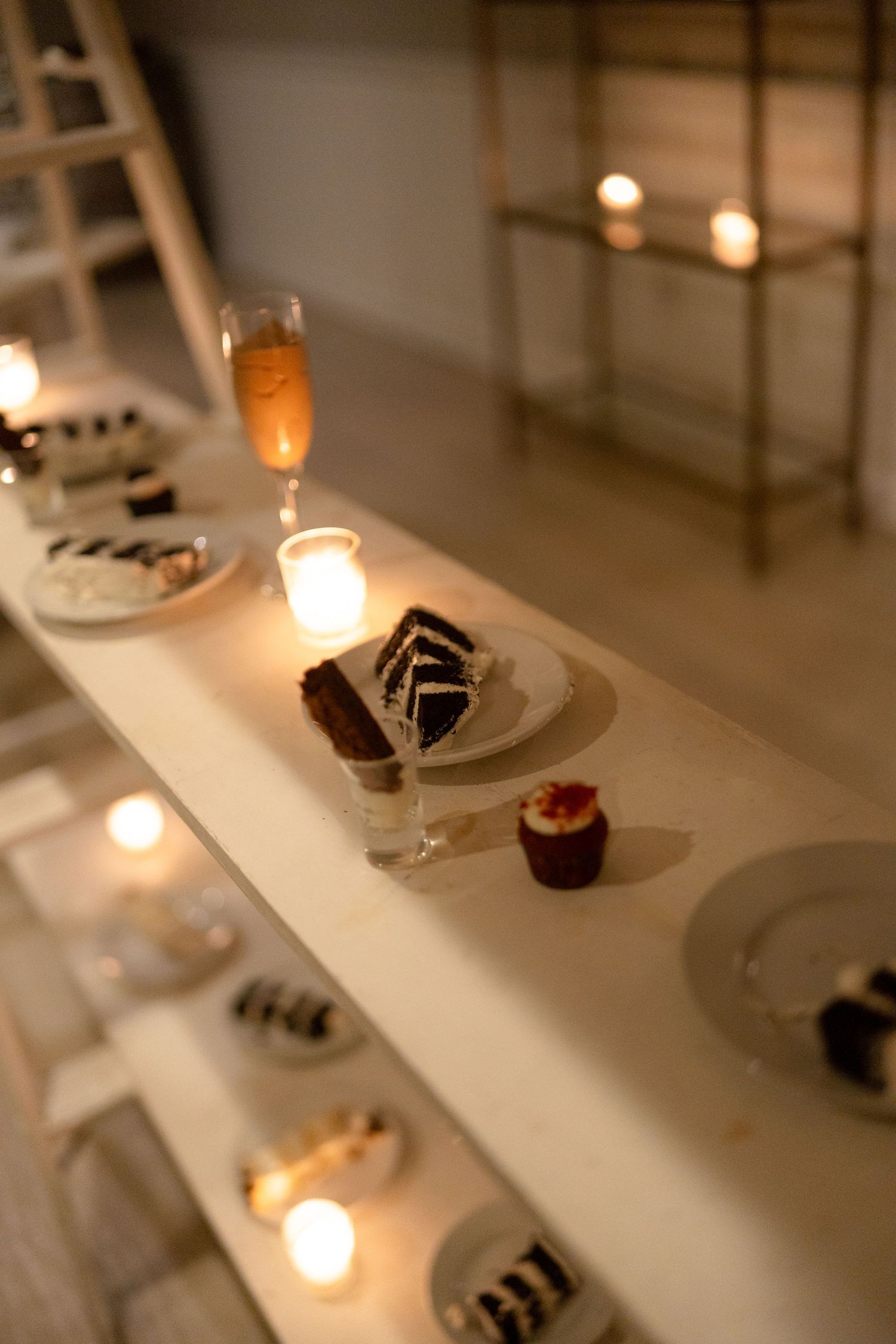Candlelit dessert display with chocolate cake slices, cupcakes, and champagne glasses at a wedding reception.