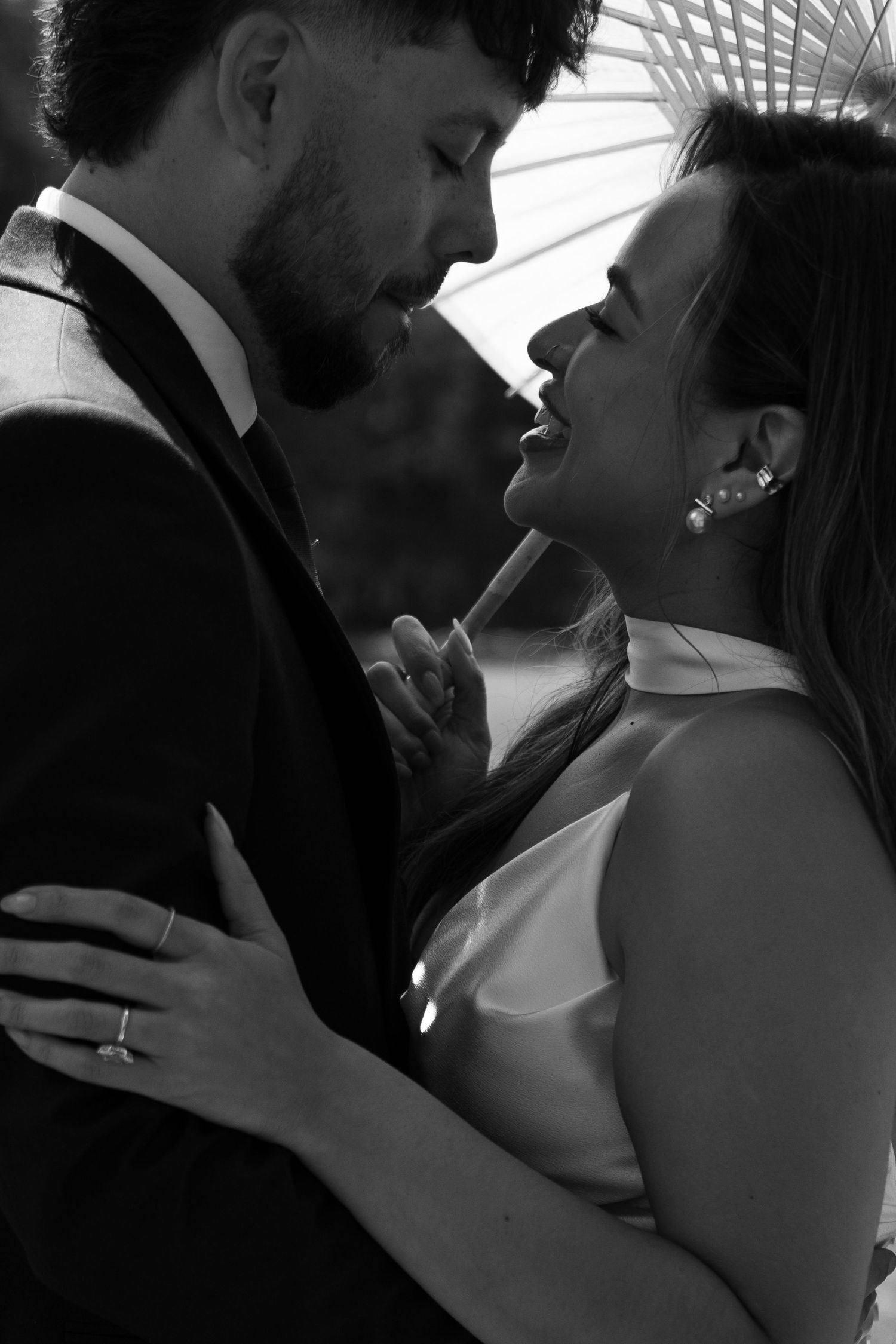 A black and white close-up of a bride and groom sharing an intimate moment under a white parasol.