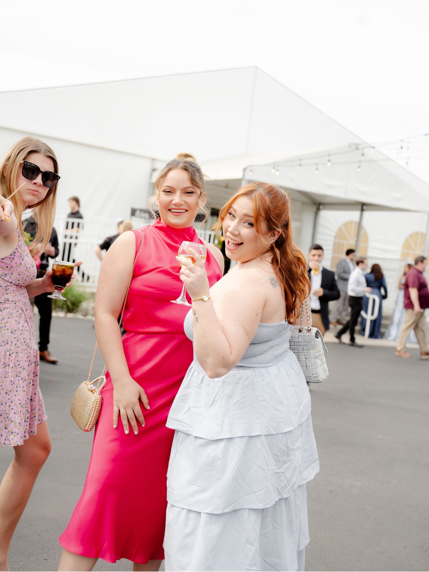 Three friends in colorful dresses share a laugh at an outdoor event.