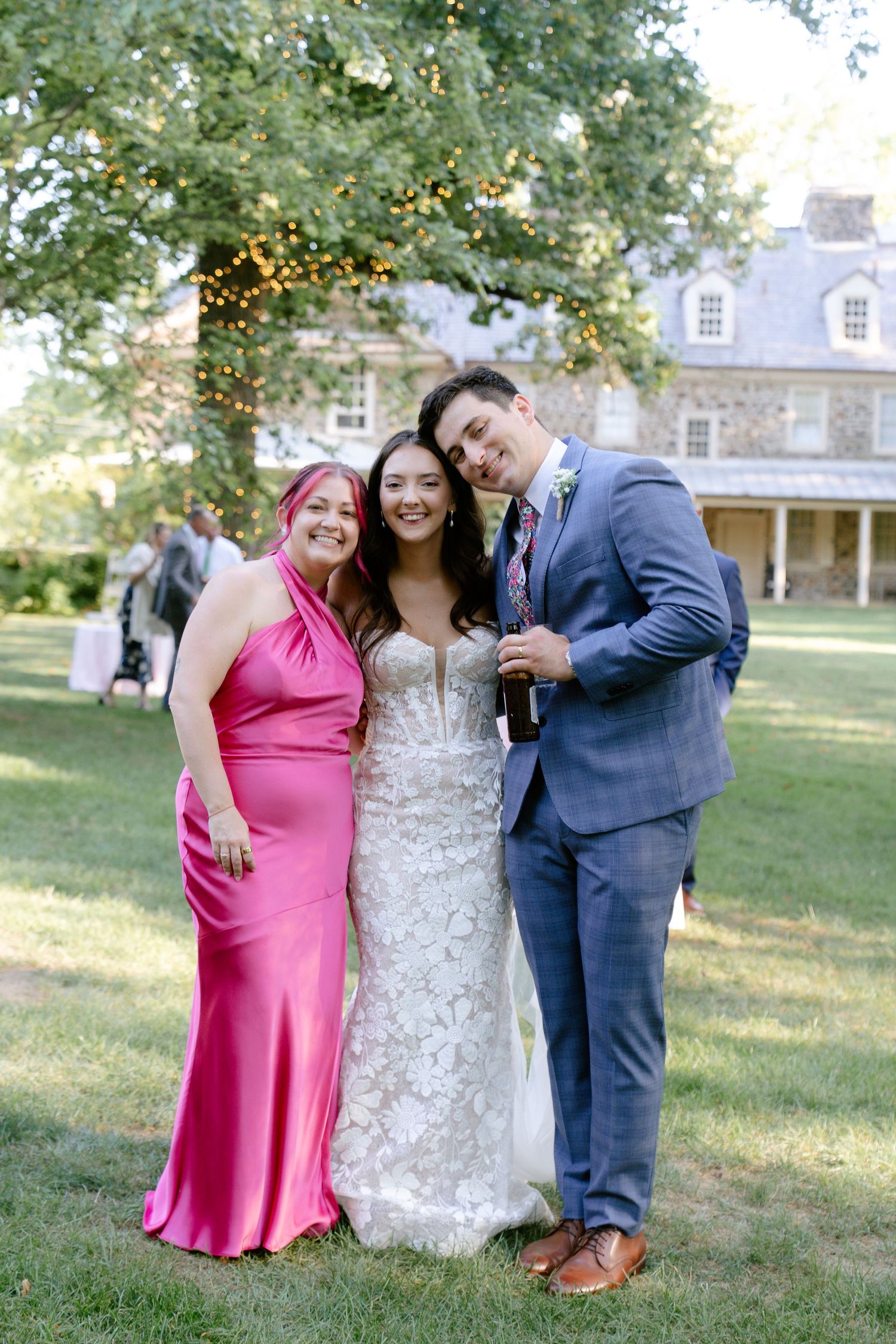 Wedding party poses for photos on a sunny lawn with historic buildings in the background.