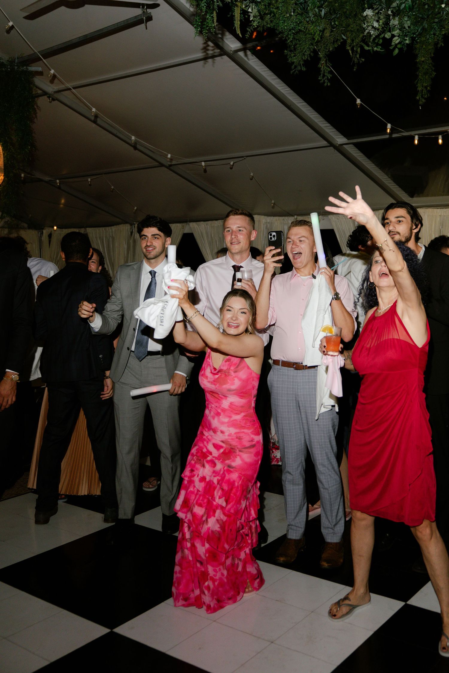 Wedding guests dancing and celebrating at nighttime reception under tent lighting.