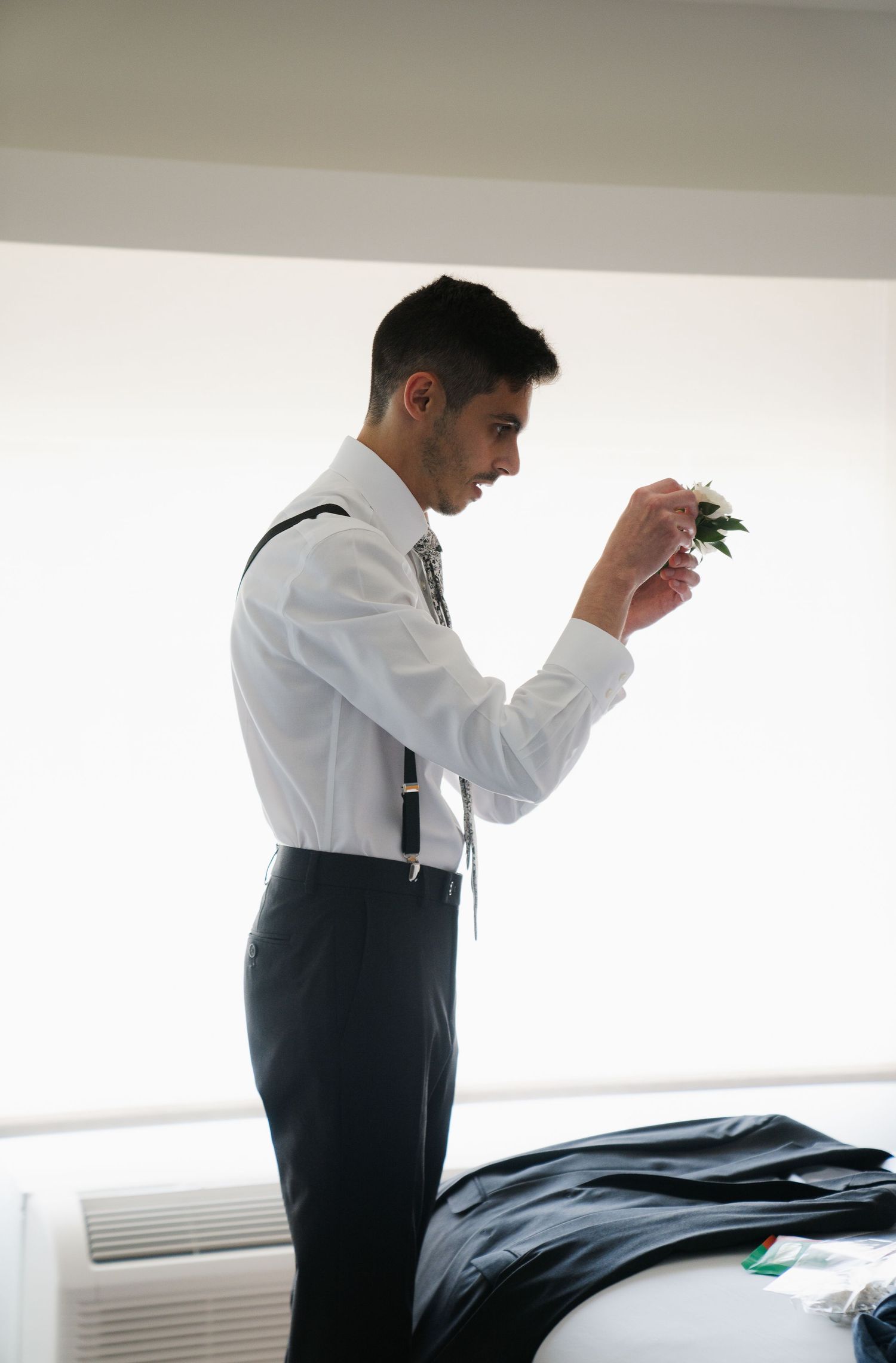 A person in a white dress shirt and dark vest stands in profile against a white wall.