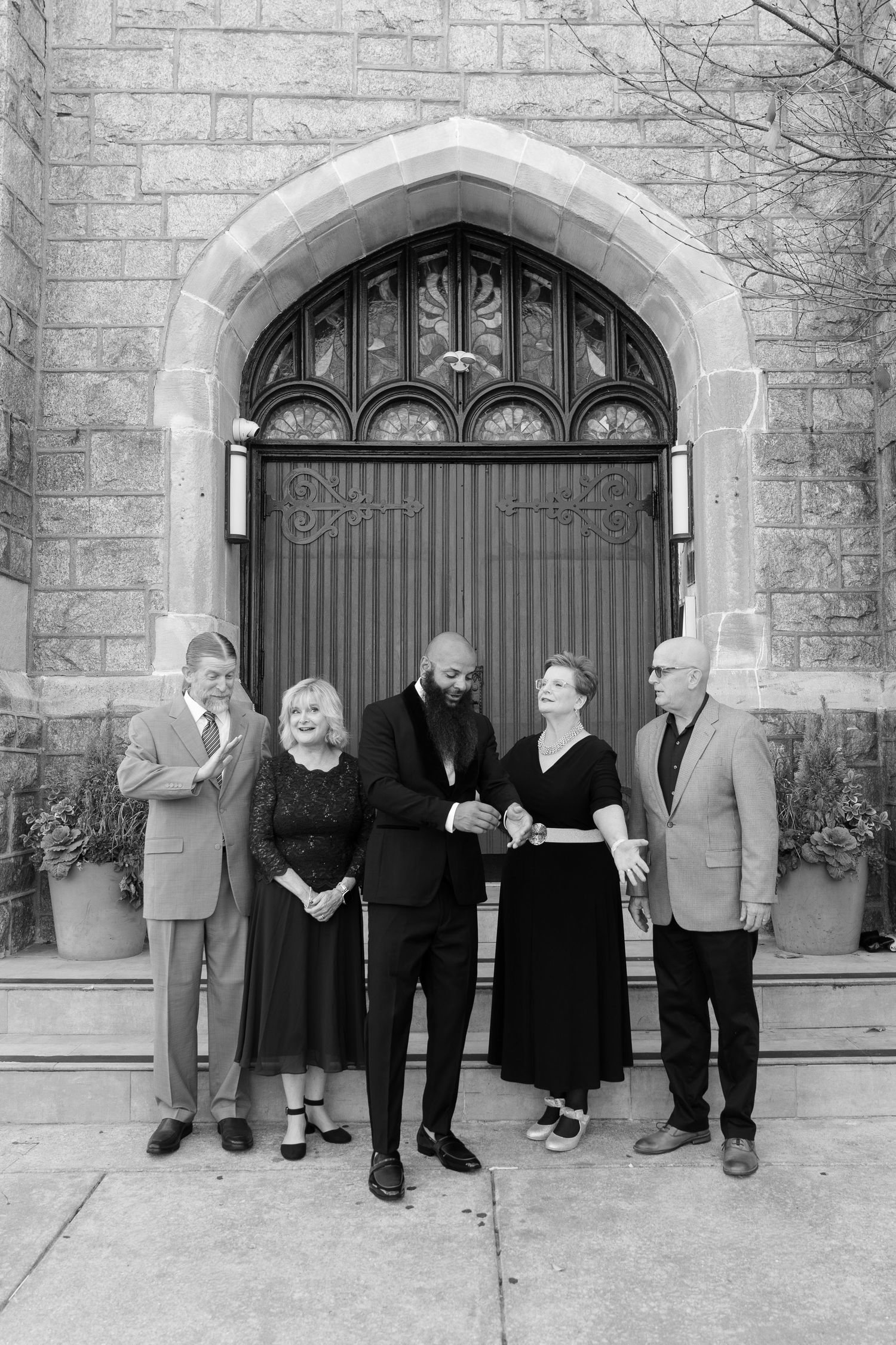 Wedding party poses in front of gothic church doorway in black and white photography.