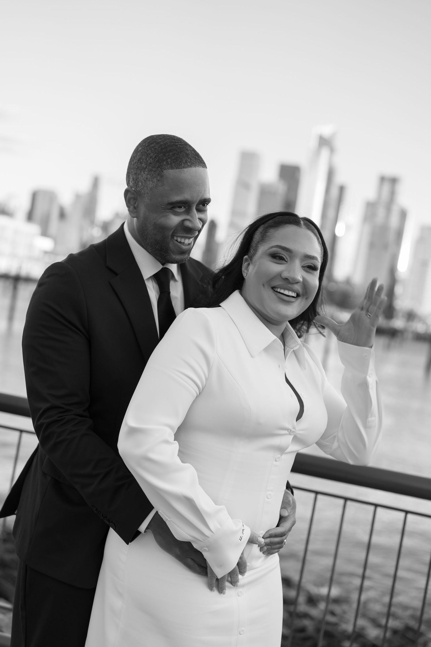 A couple shares a candid moment against a city skyline backdrop in black and white.
