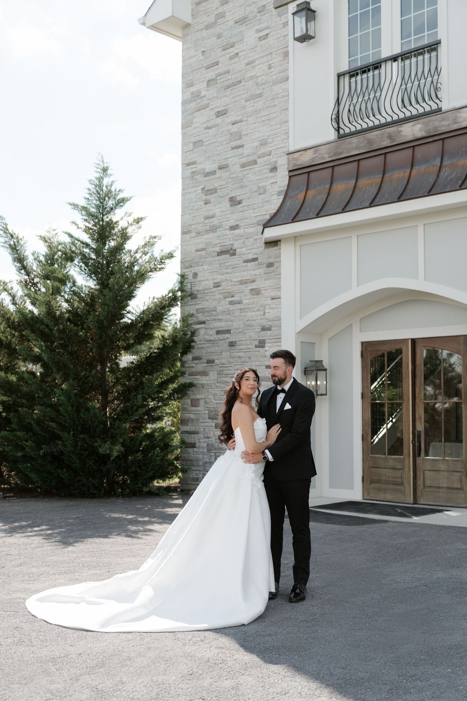 Bride and groom embrace outside elegant stone wedding venue with bride in flowing white gown.