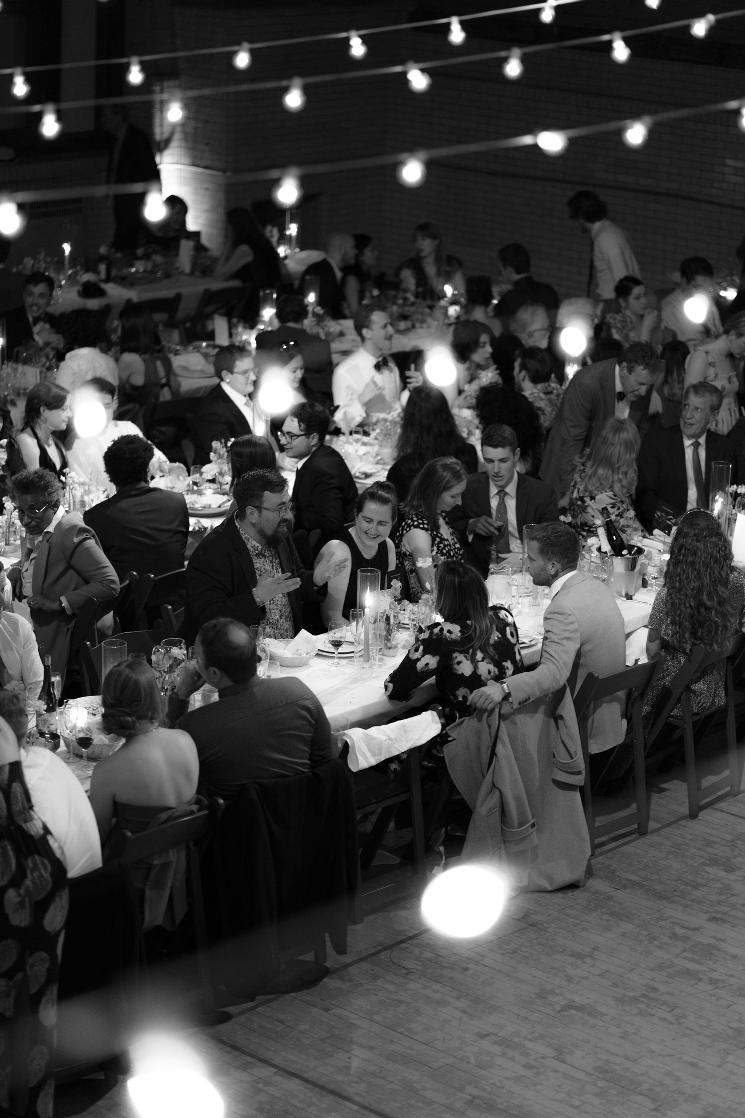 Wedding guests enjoy dinner under string lights at an elegant outdoor reception.