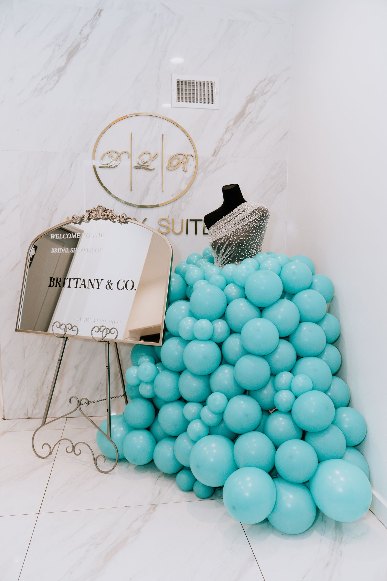 Decorative display of Tiffany blue balloons and luxury brand signage on marble background.