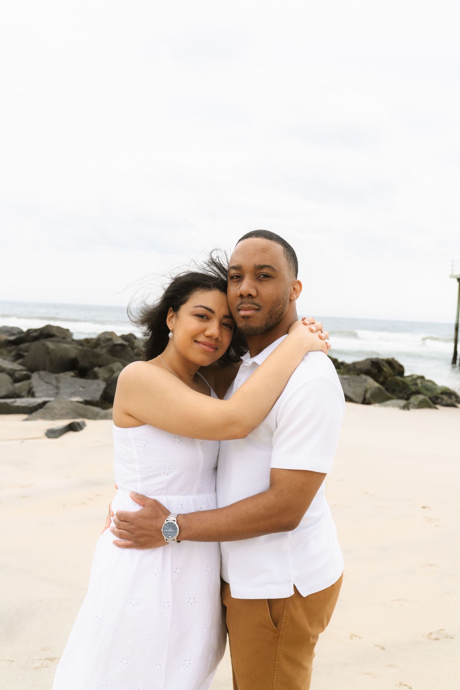 A couple in white outfits shares tender moments on a rocky beach.