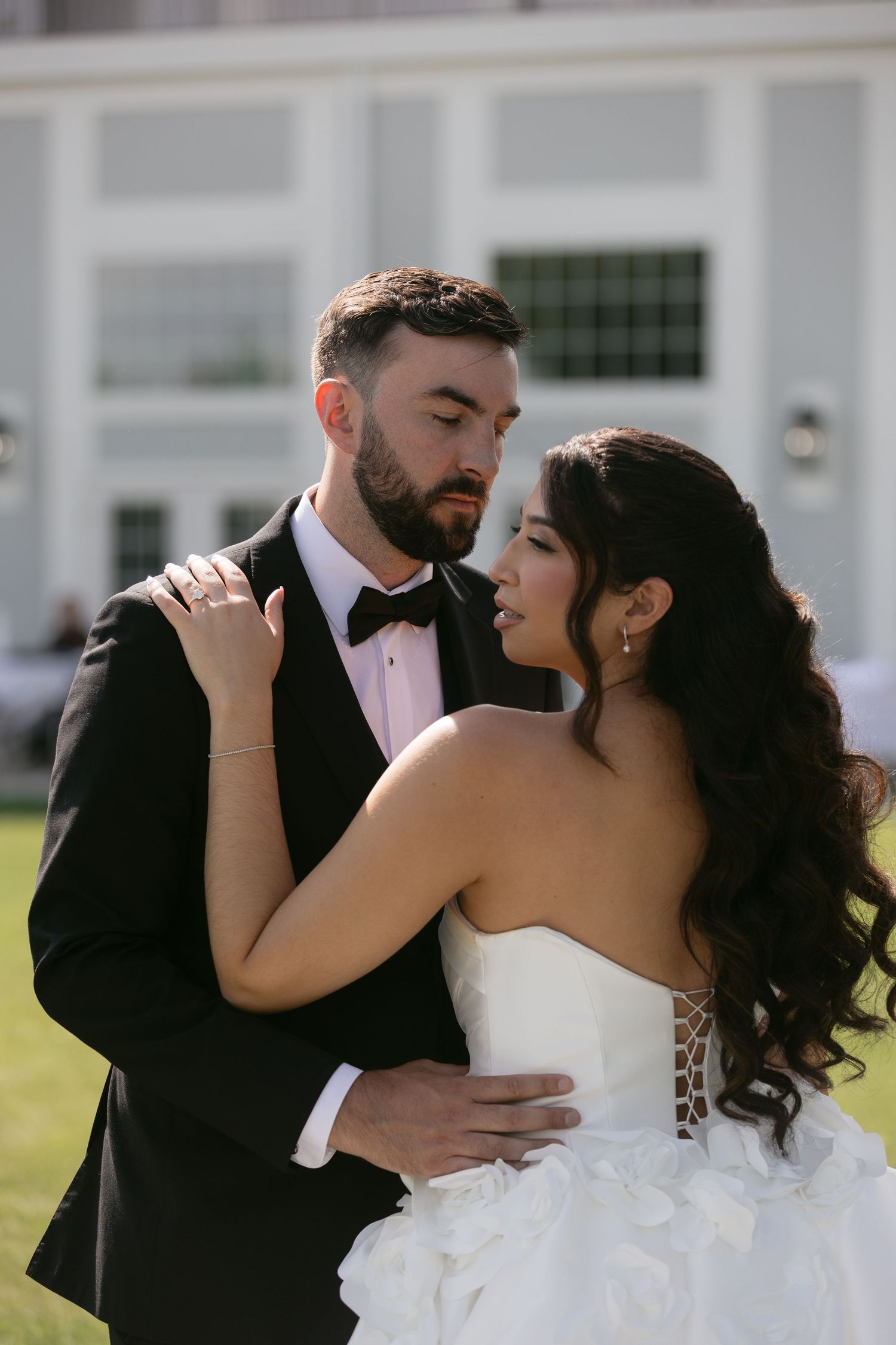 Bride and groom share an intimate moment outdoors, groom in black tuxedo and bride in strapless gown.