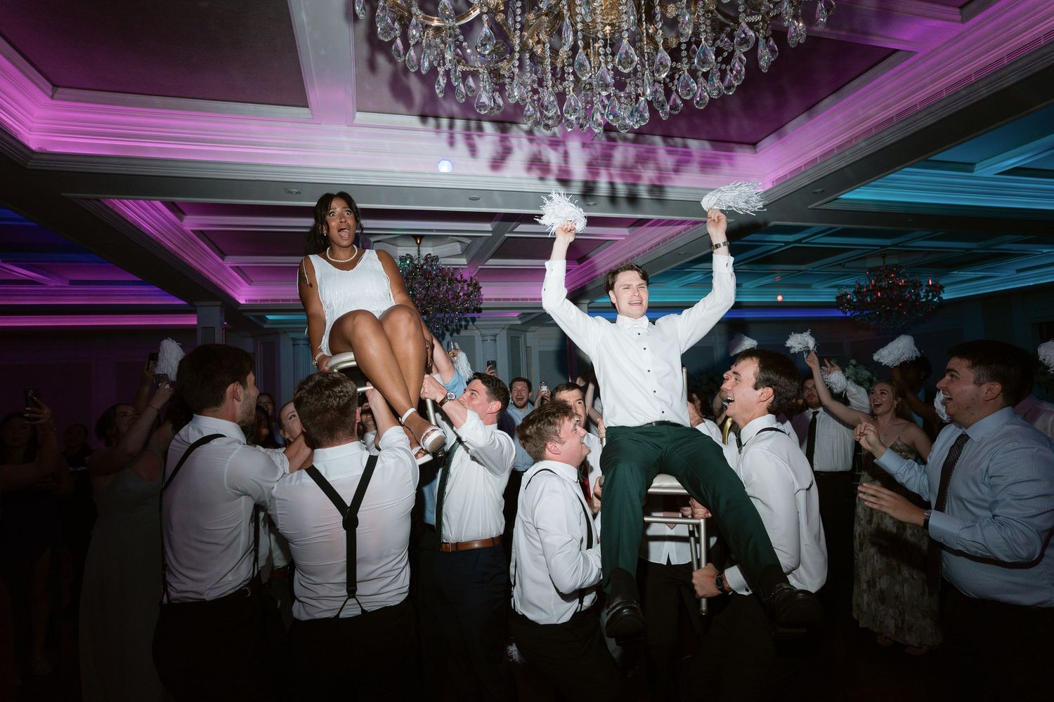 Bride and groom lifted by groomsmen on a elegant wedding reception dance floor with chandeliers.