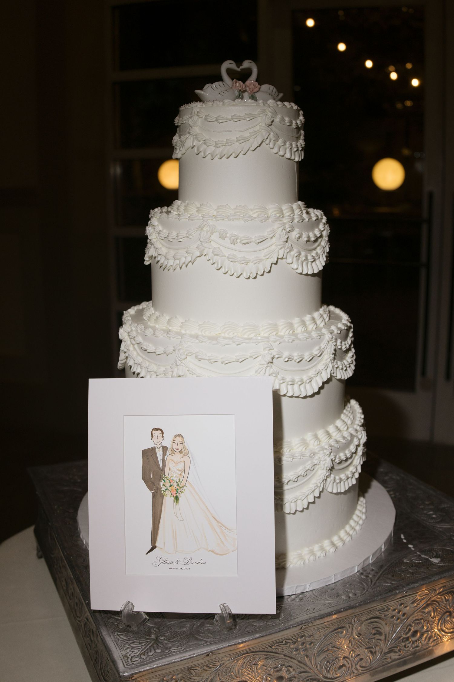Four-tier white wedding cake with ruffled frosting and heart topper beside an illustrated bride and groom portrait card.