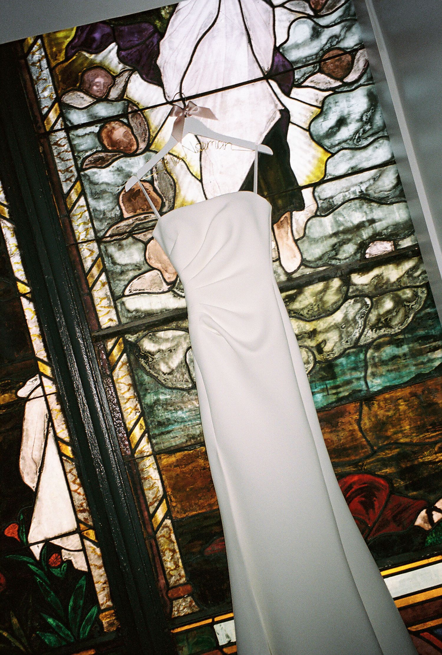 Elegant white wedding dress displayed against a stained glass window backdrop in a church.
