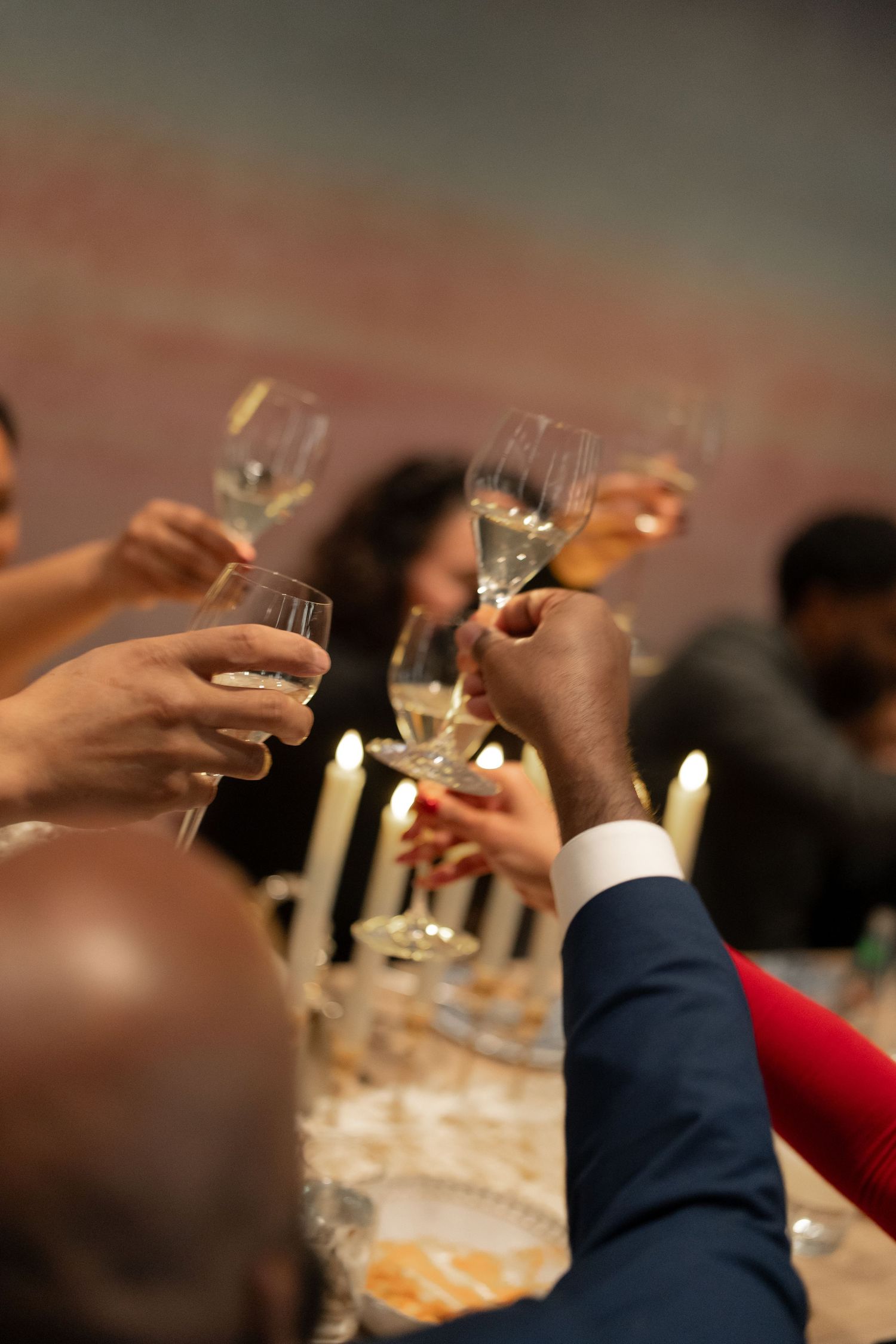 Multiple hands raise champagne glasses in a celebratory toast during an elegant wedding reception.