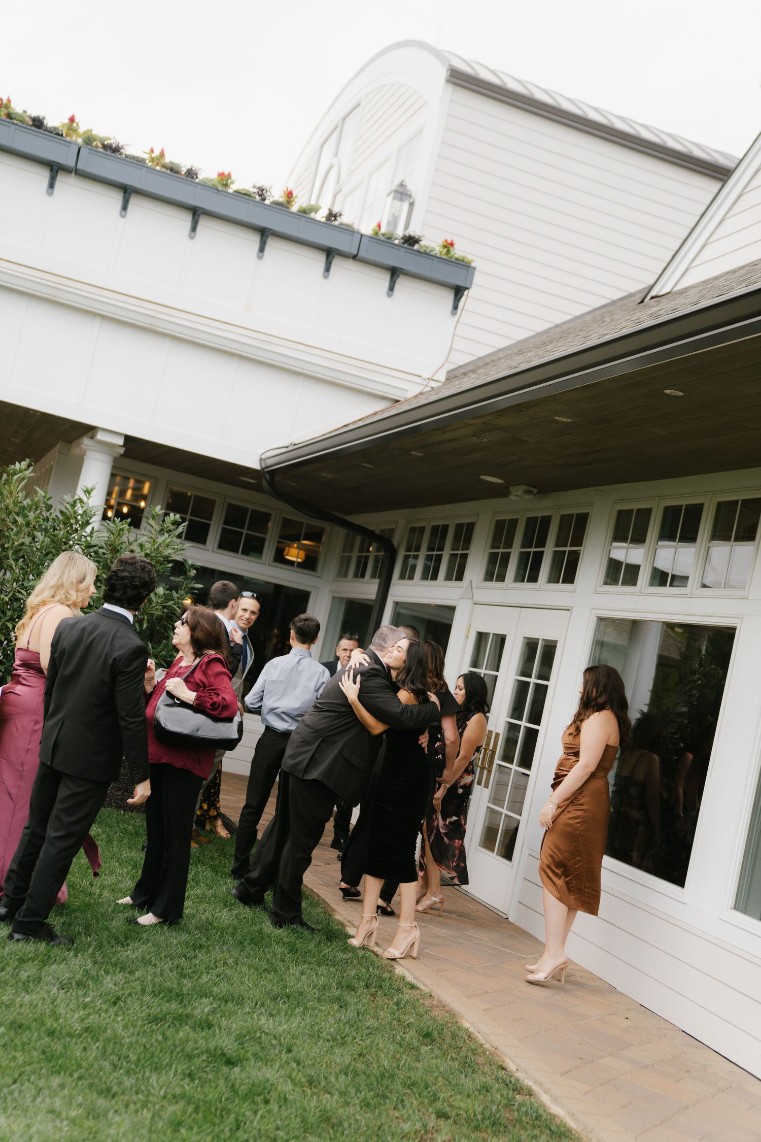 Wedding guests gather outside a white building for an elegant outdoor reception event.
