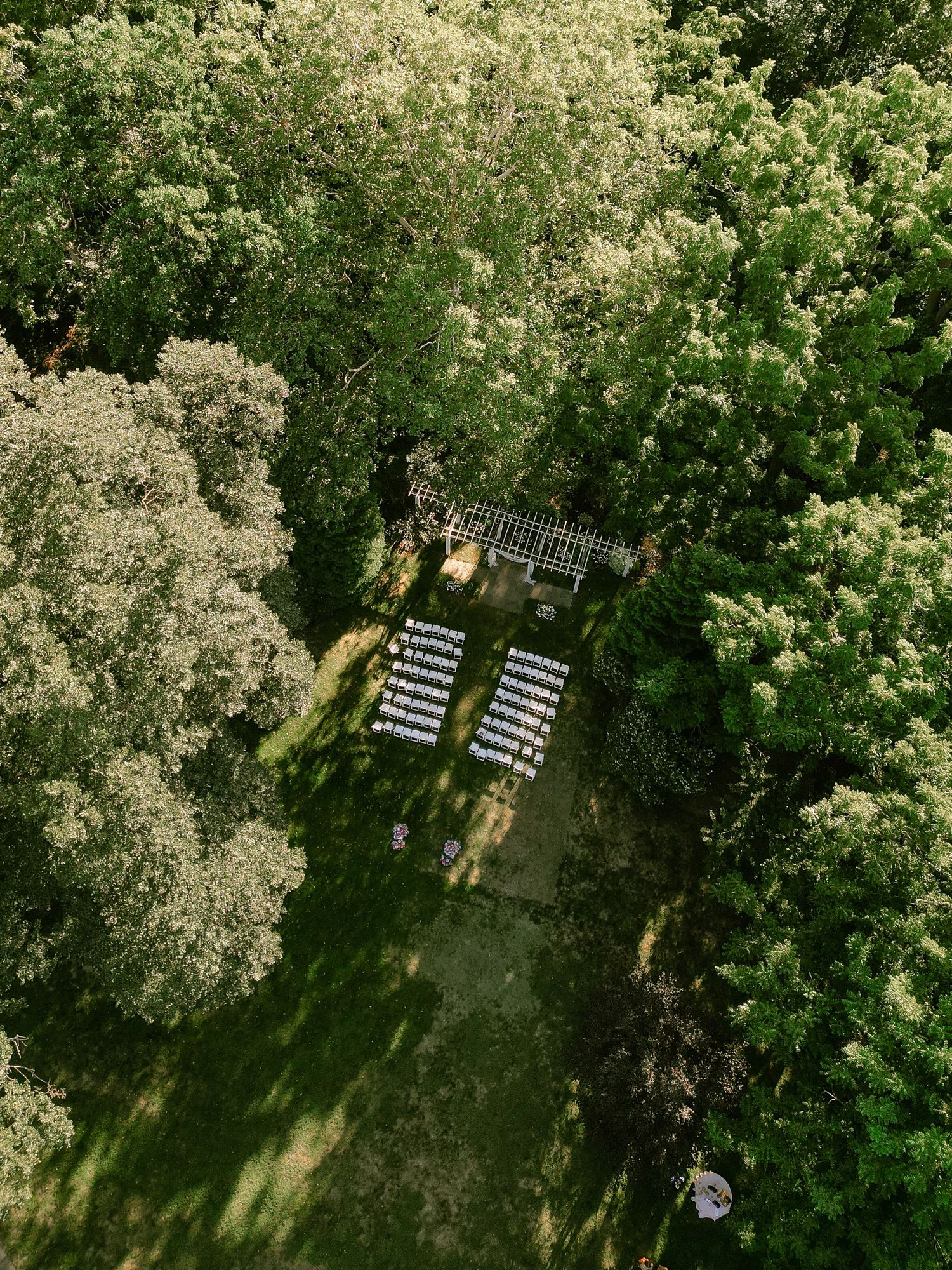 Aerial view of an outdoor wedding ceremony setup surrounded by lush green trees.