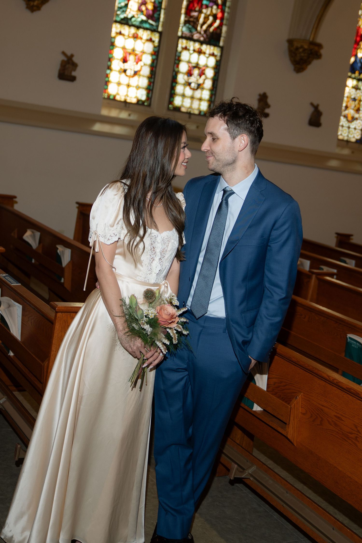 A couple in formal attire shares a moment between wooden church pews.