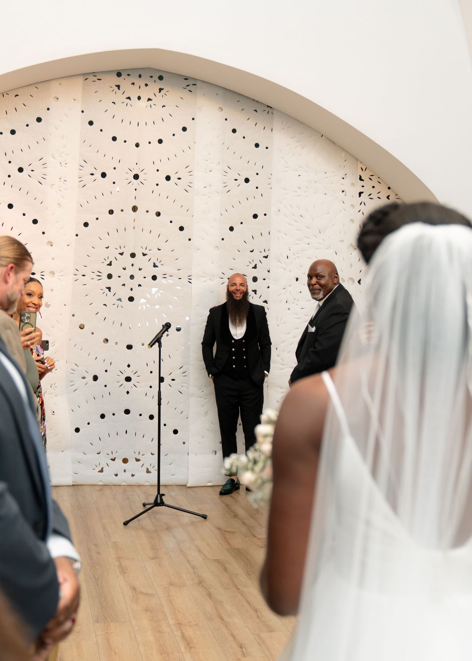 Wedding ceremony moments captured against a white wall with decorative black dot pattern.