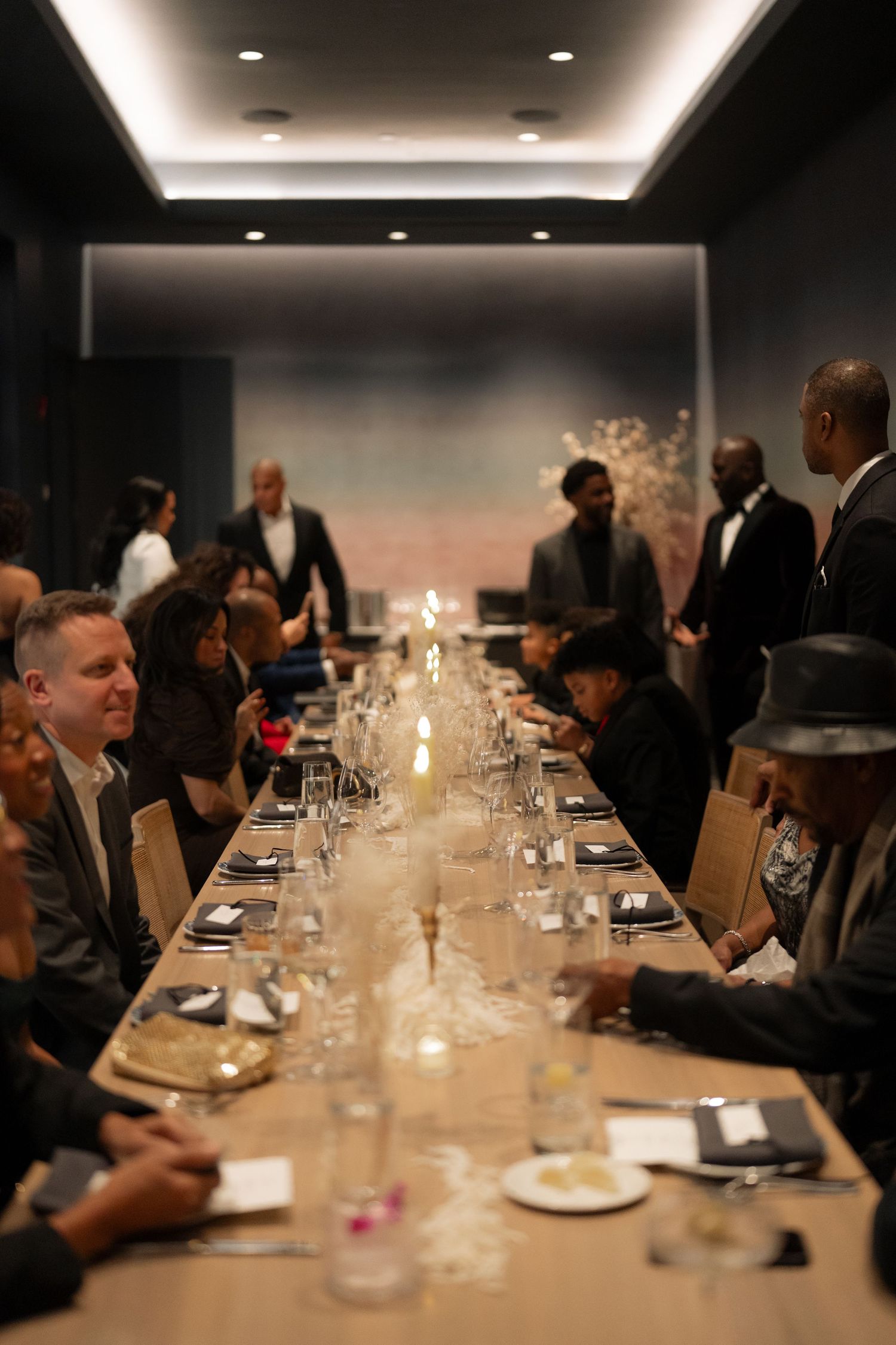 Elegant dinner party setting with long table, candles, and guests seated in a dimly lit room.