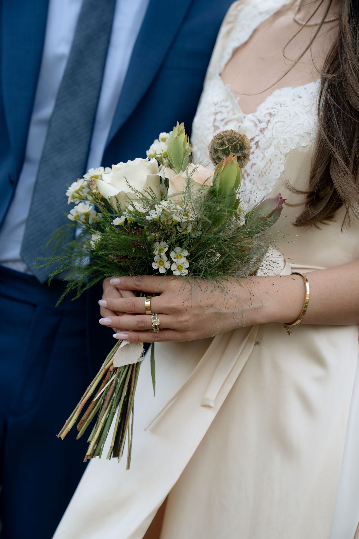 Close-up view of a bridal bouquet with white flowers and greenery held against a cream-colored dress.